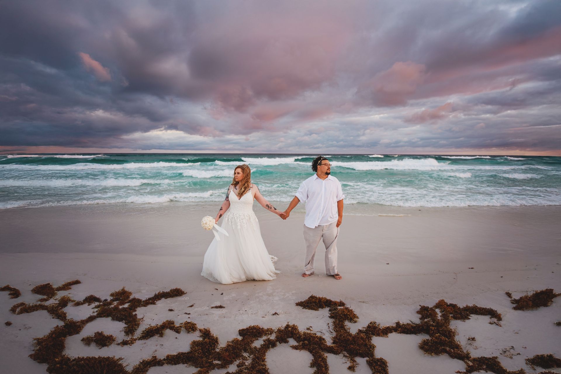 bride and groom holding hands under moody clouds during 30A beach wedding