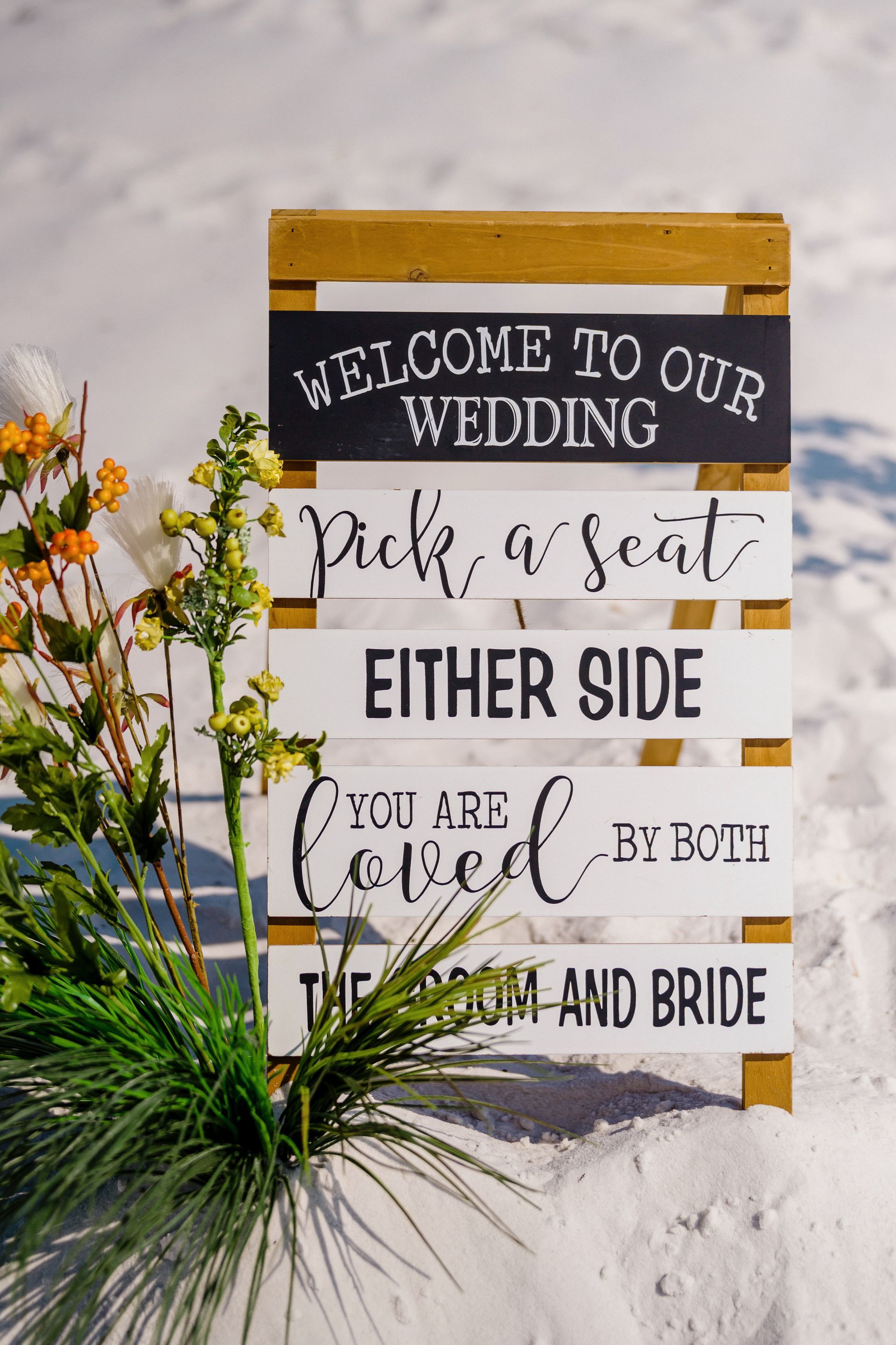 Wedding welcome sign on easel with black-and-white text and flowers in a snowy outdoor setting