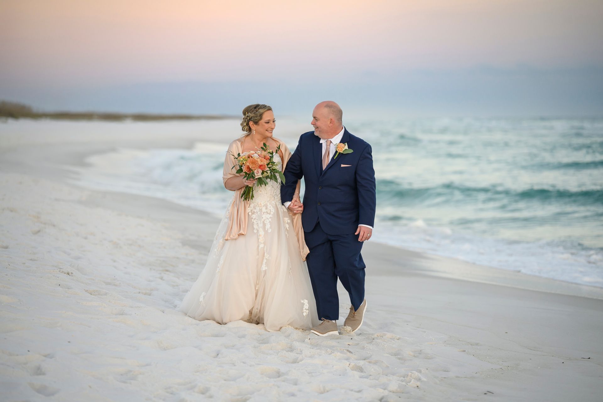 Bride and groom walking hand in hand on a beach at sunset