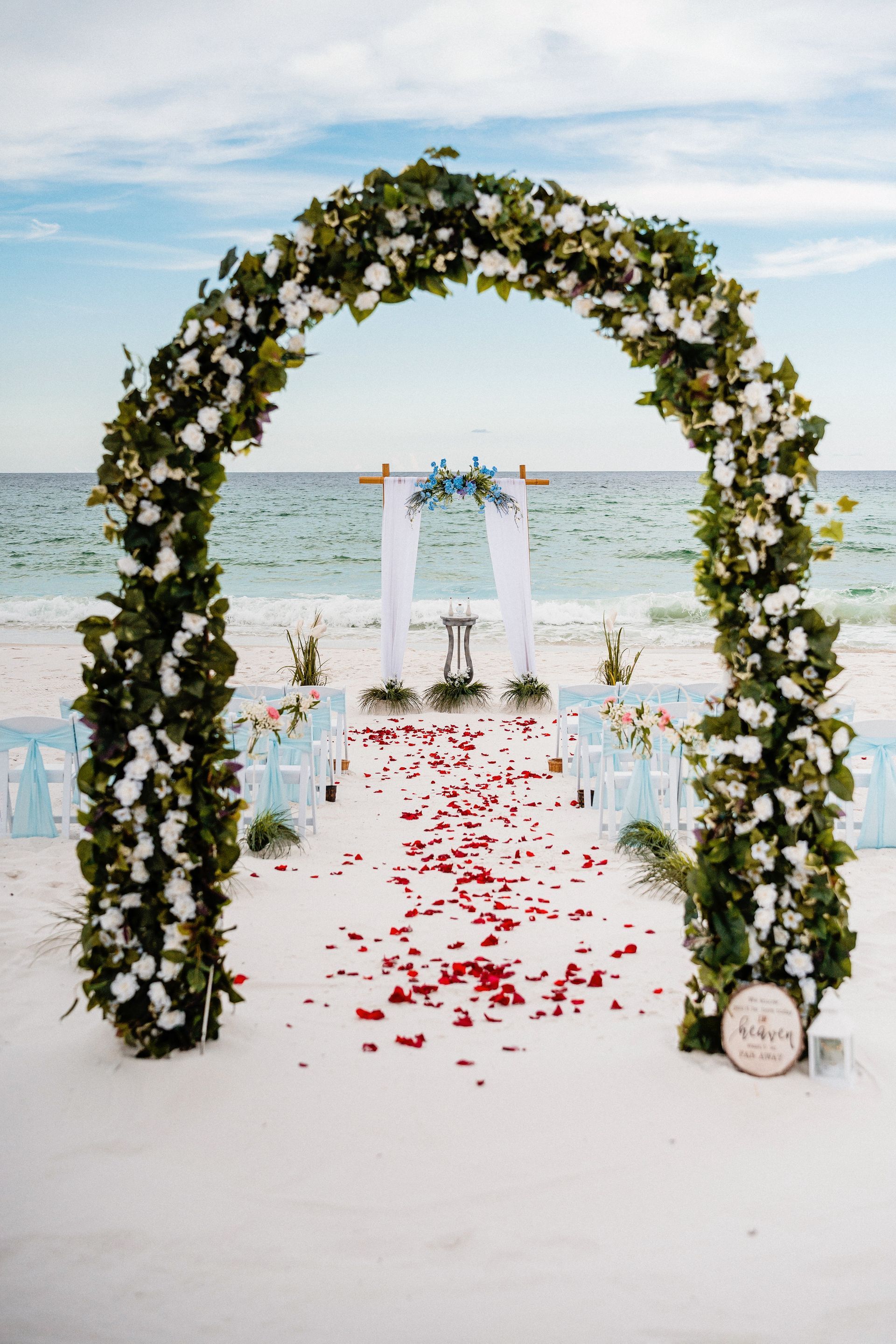 Beach wedding arch with white flowers and red petals by the sea