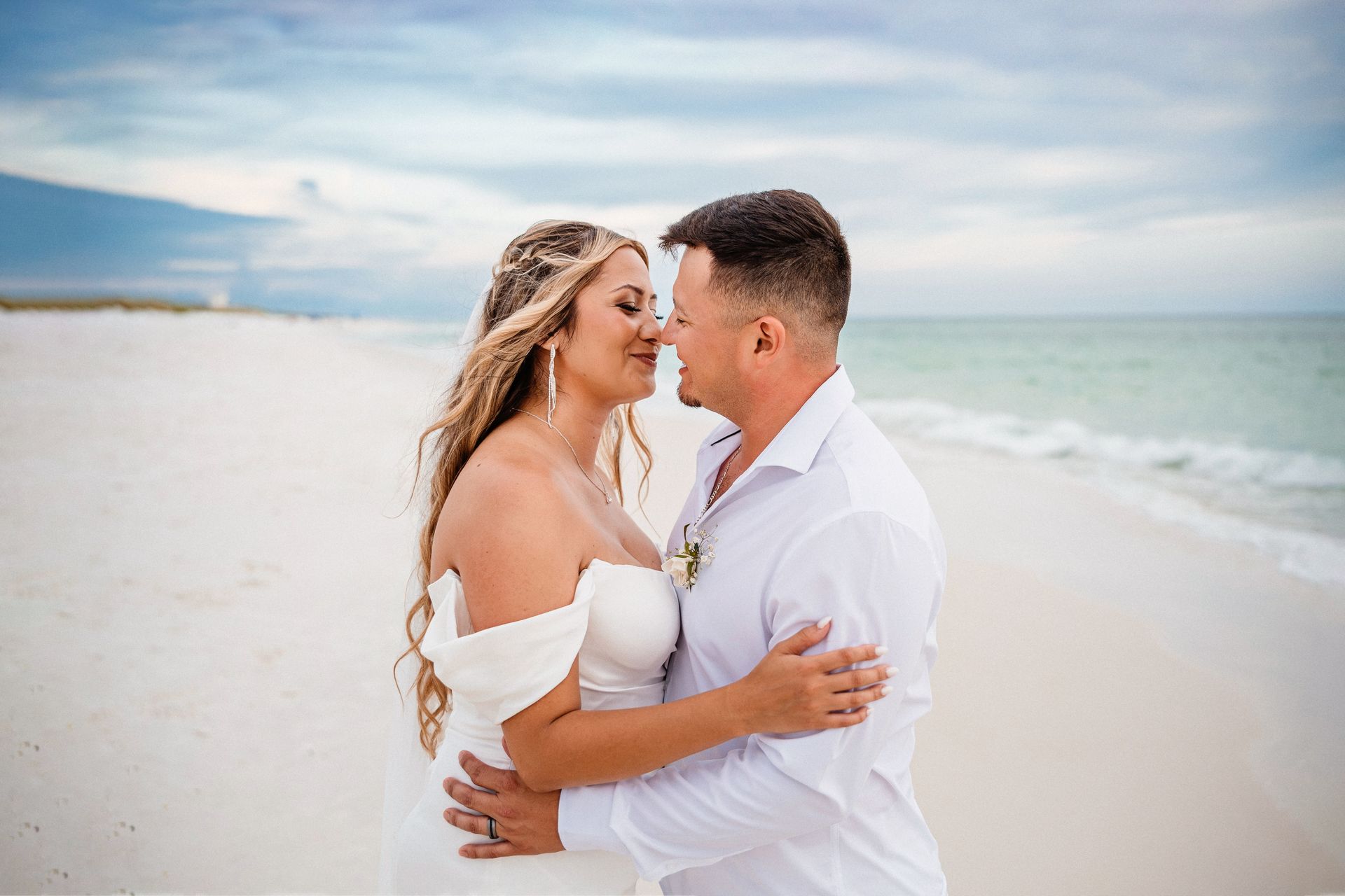 Couple embracing on a white-sand beach at sunset, with the ocean in the background