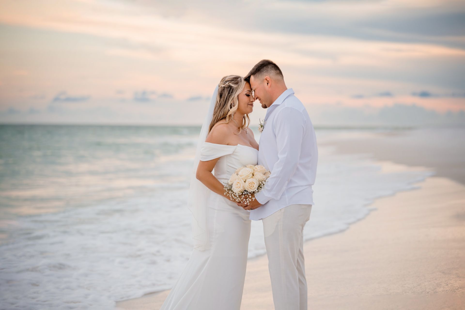 Bride and groom embracing on a beach at sunset with ocean waves behind them