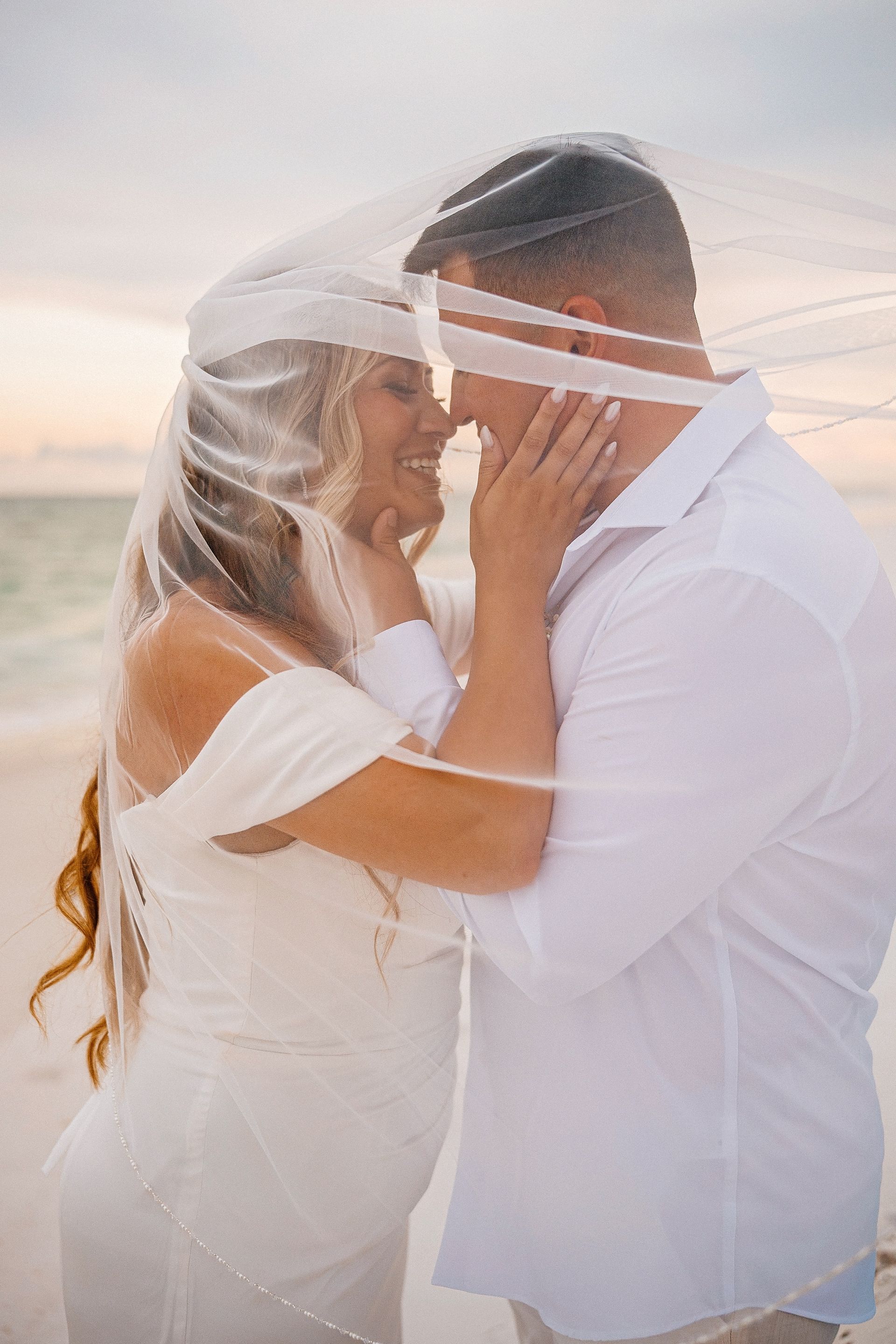 Couple in white embracing on a beach at sunset