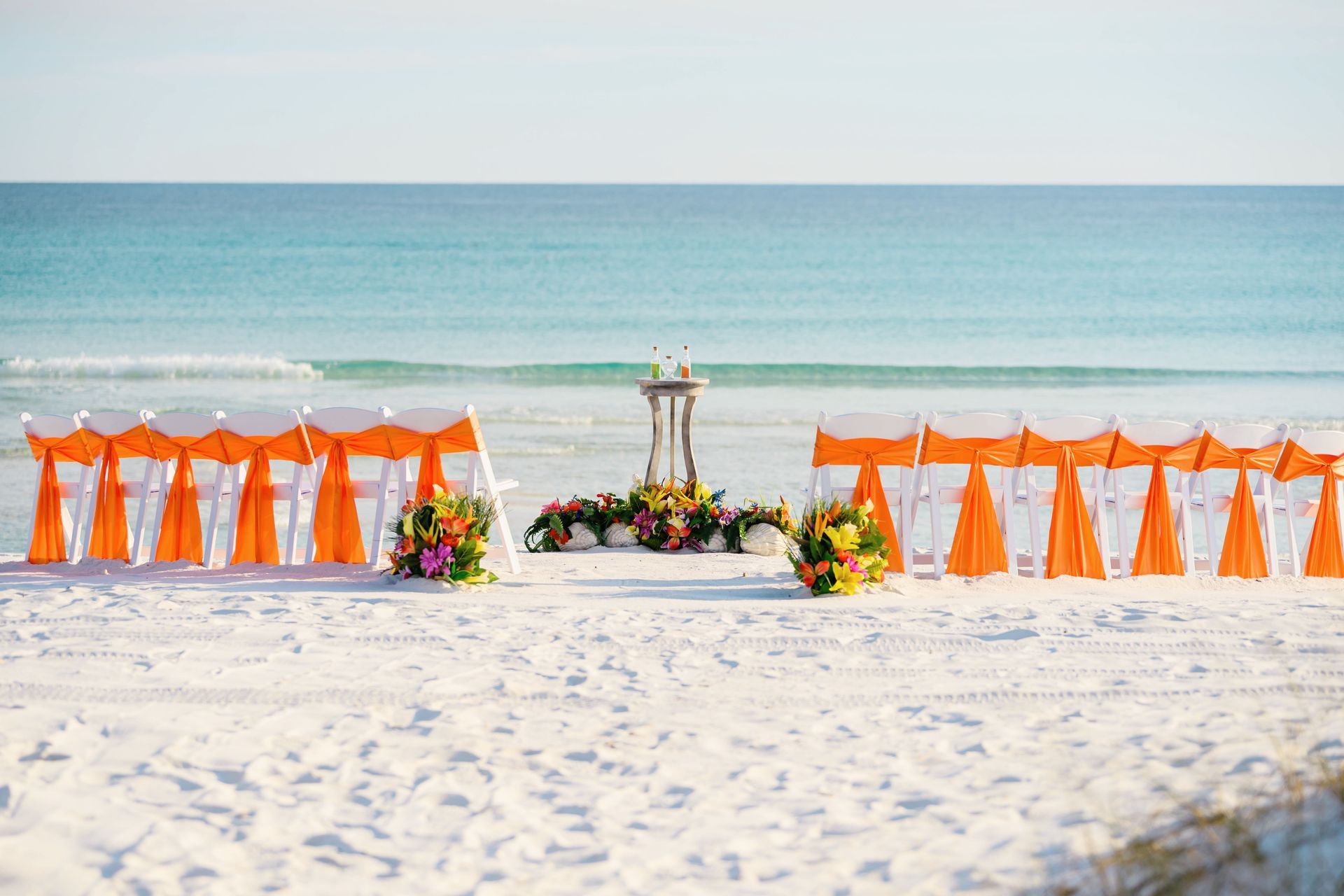 Beach wedding setup with orange chairs, floral arch, and ocean backdrop