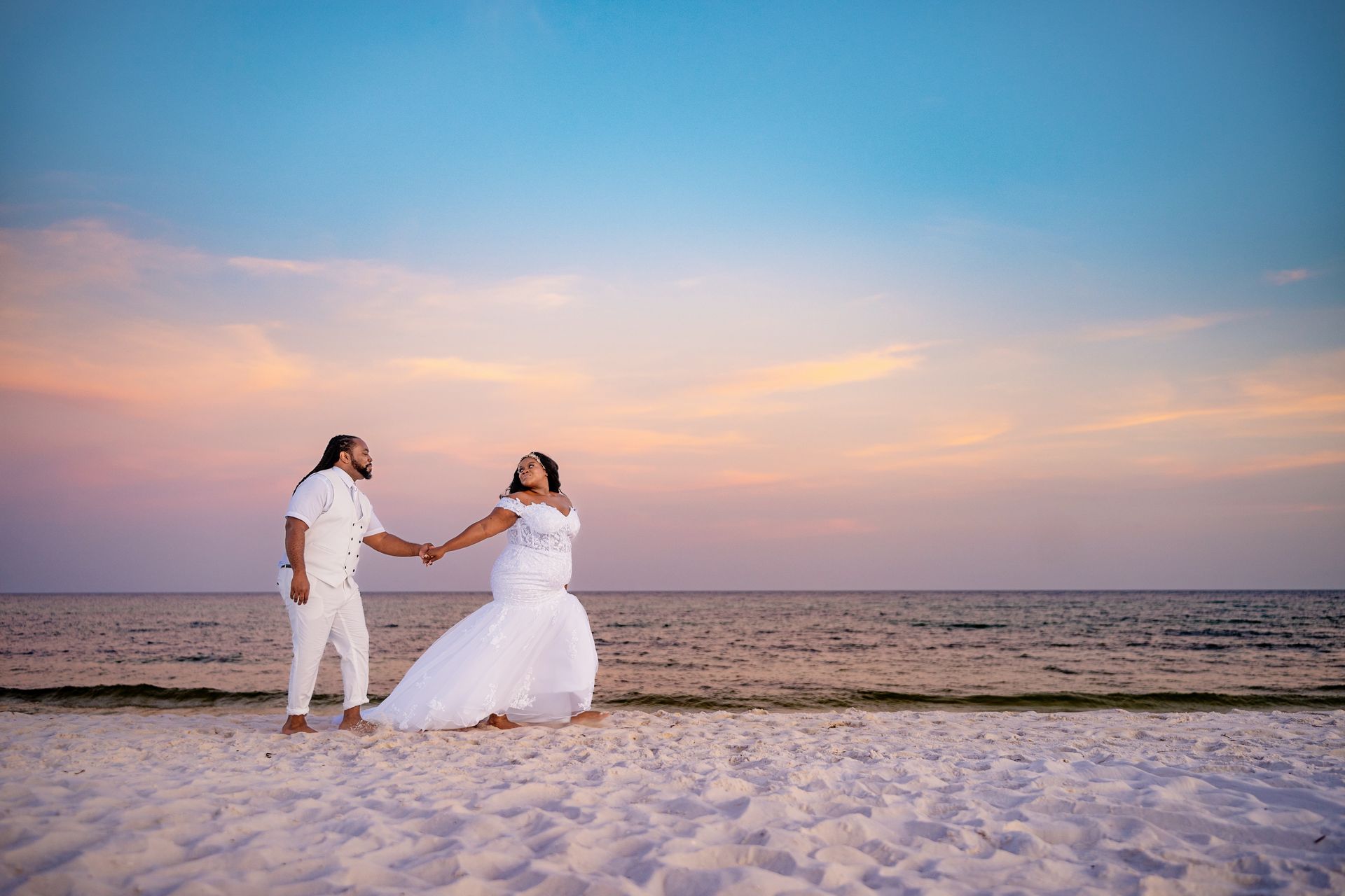 bride and groom holding hands and walking on beach at sunset