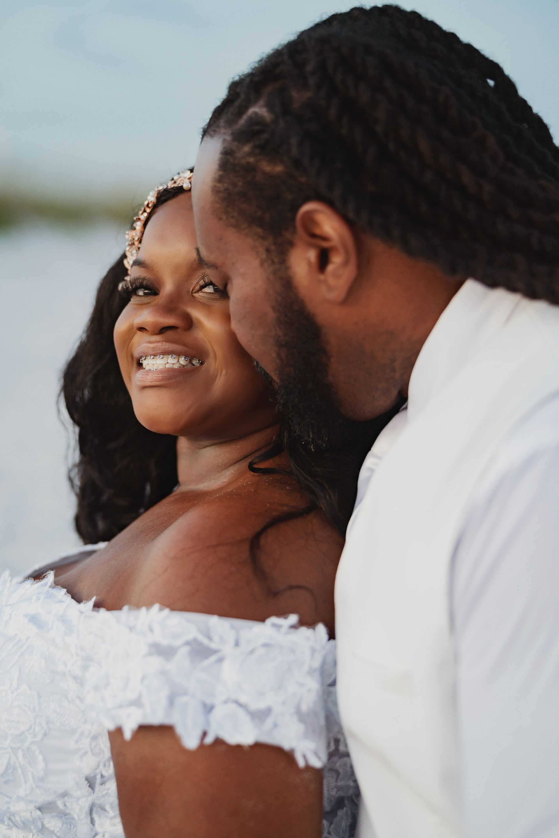 Couple in white wedding attire sharing a close moment outdoors at sunset