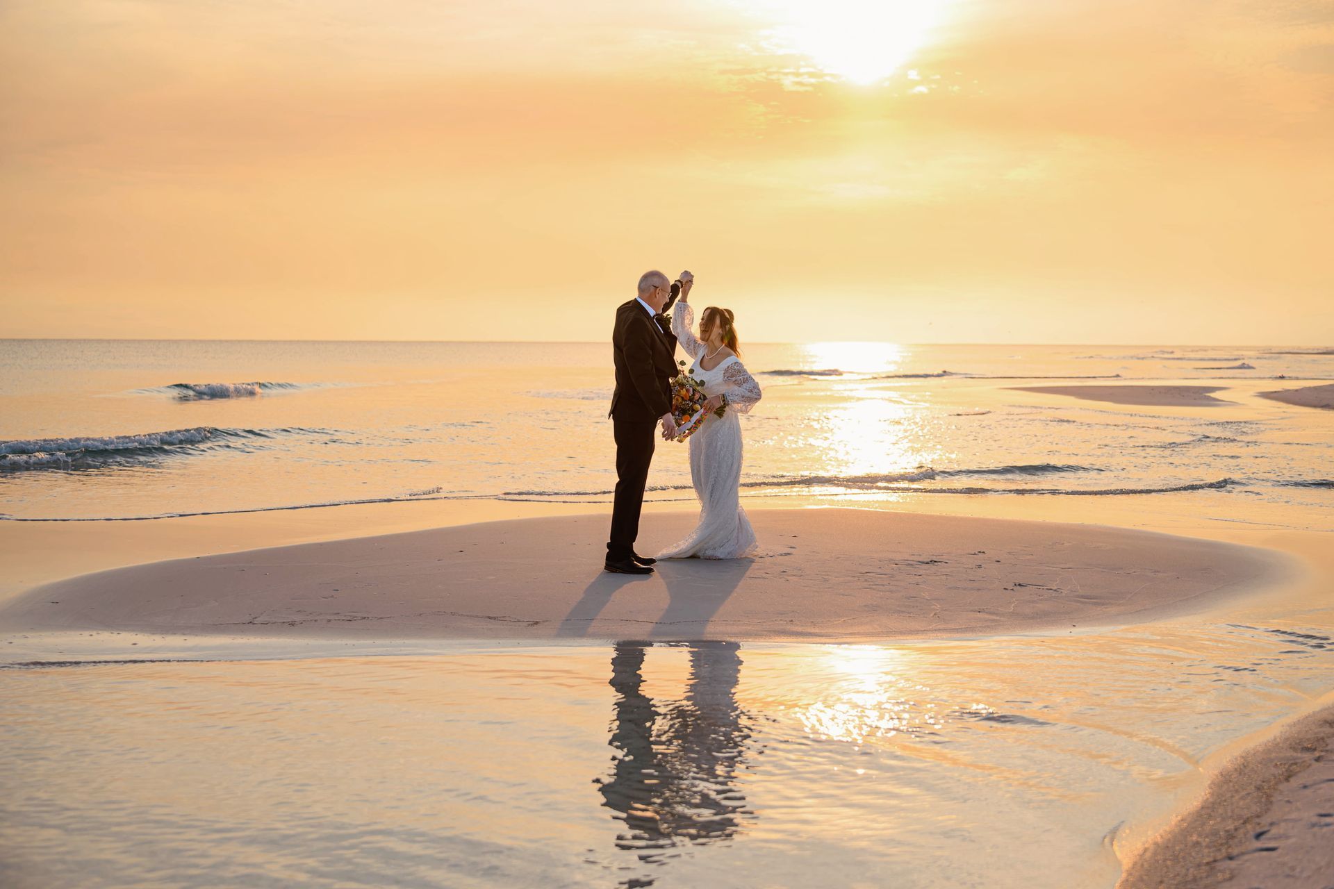 Couple standing on a beach at sunset, embracing in the warm golden light with reflections on wet sand