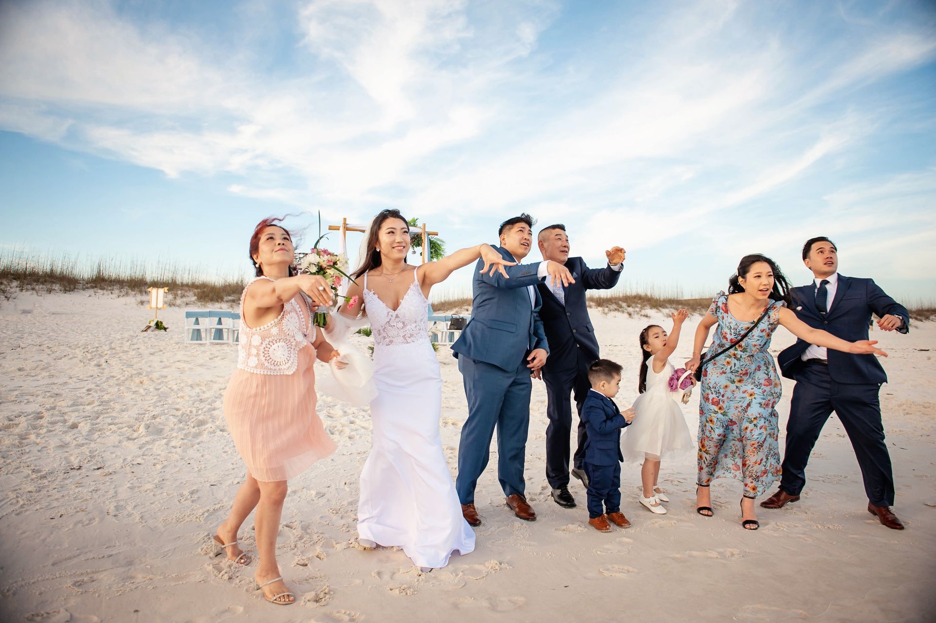 Group of friends in beach wedding attire dancing and smiling on a sandy beach at sunset