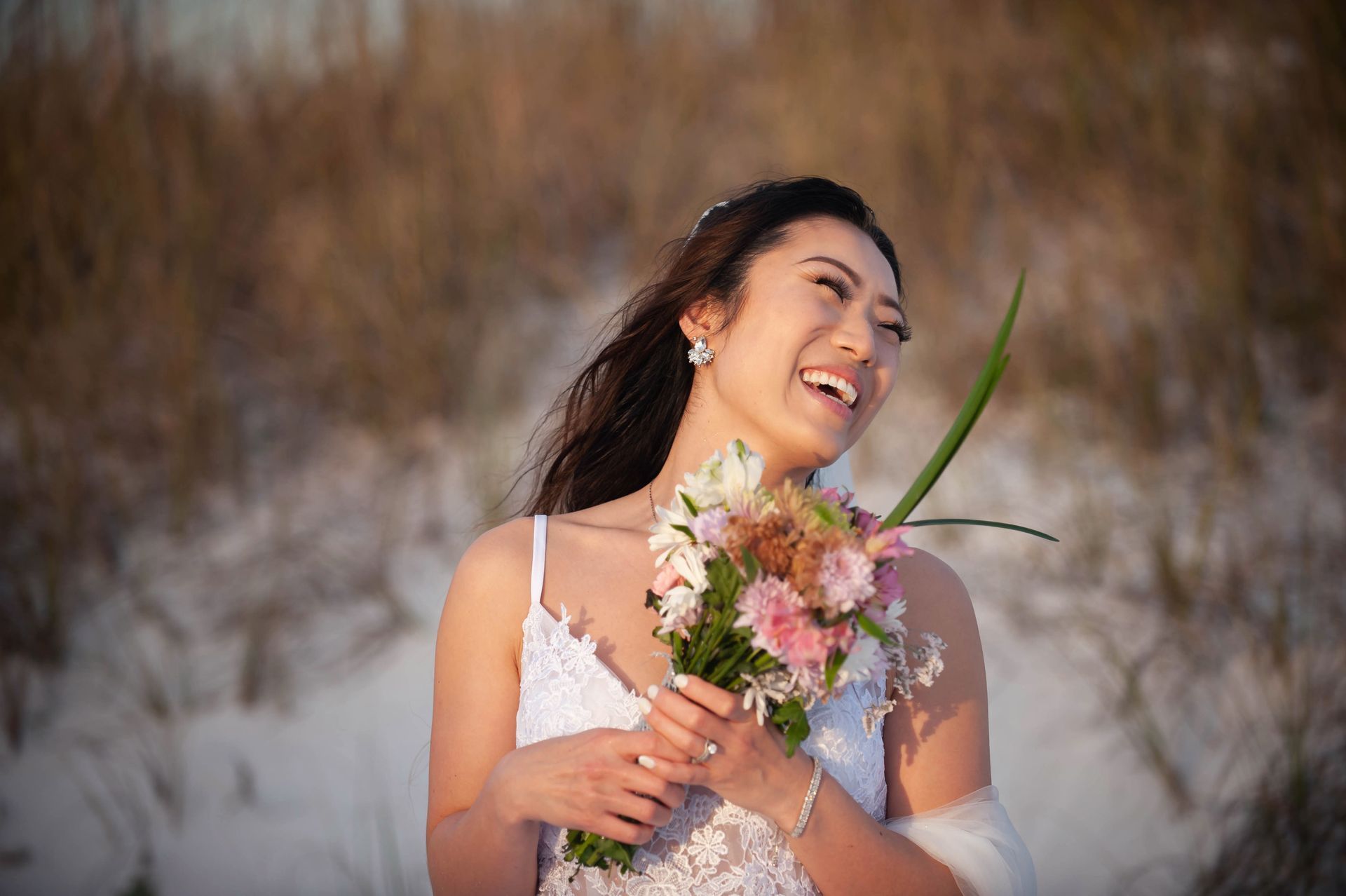 Woman in a white dress holding a bouquet, smiling in a snowy field.