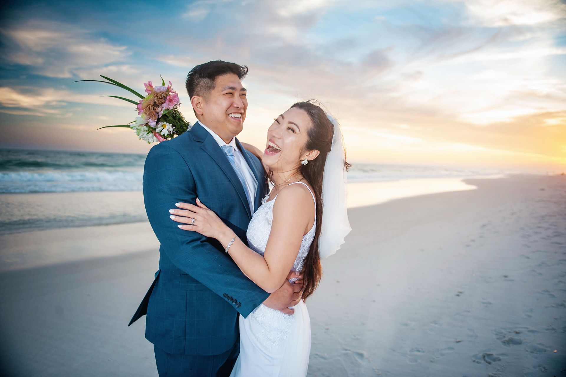 Couple embracing on a beach at sunset, with ocean waves and a pastel sky behind them
