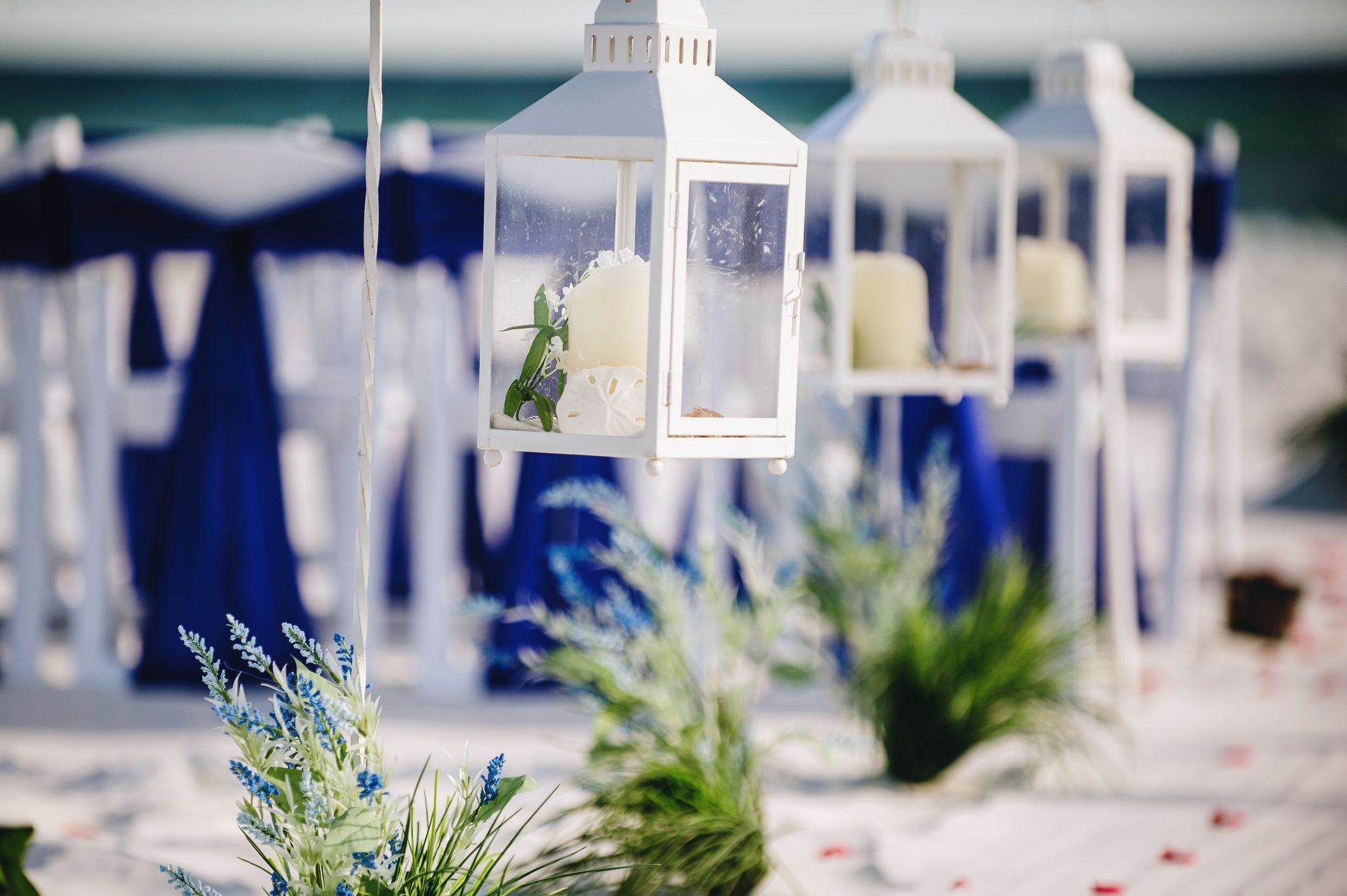 White lanterns and blue floral arrangements lining an outdoor wedding aisle with navy chairs