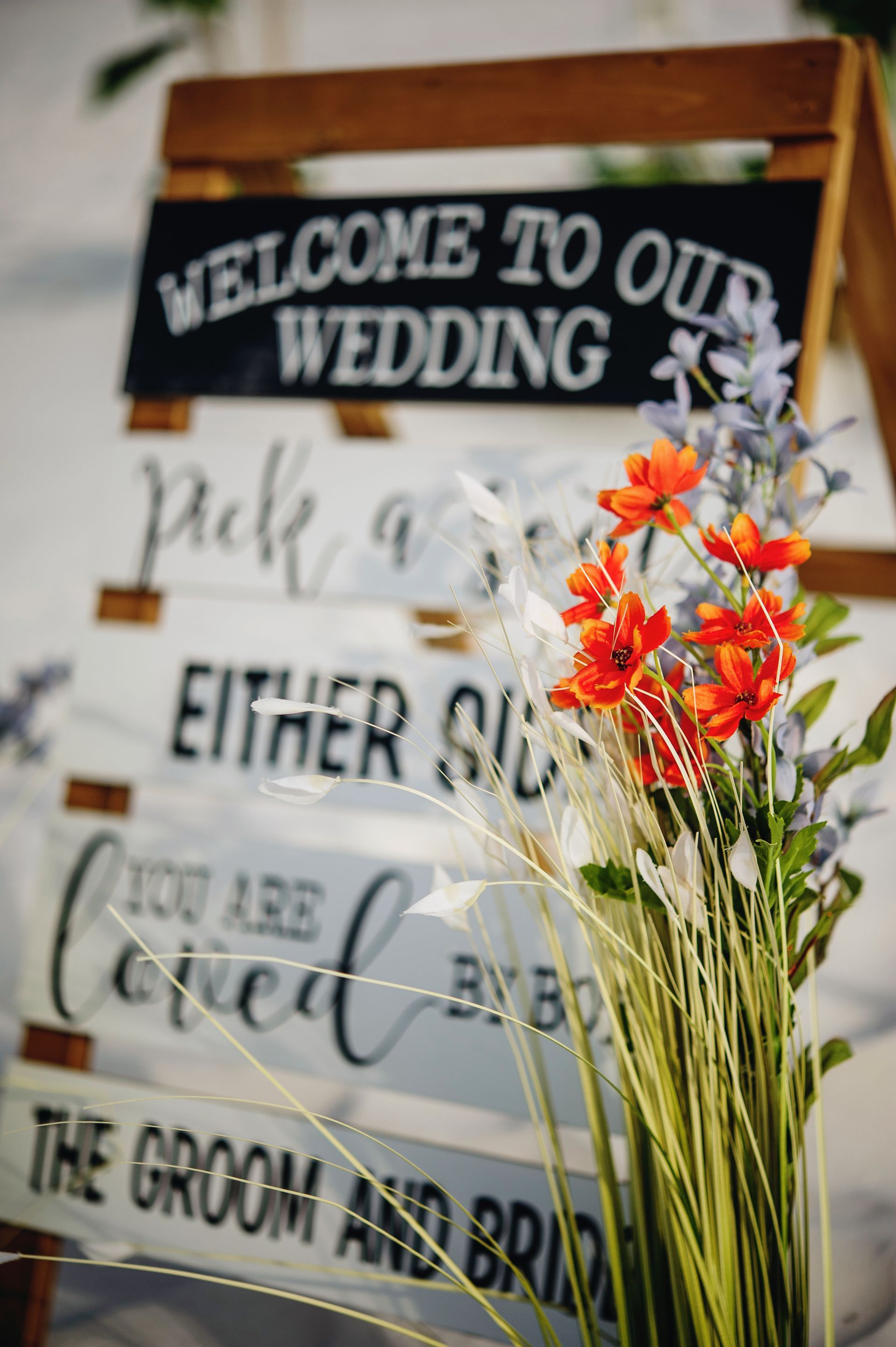 Wedding welcome sign with floral arrangement and handwritten guest directions in warm tones