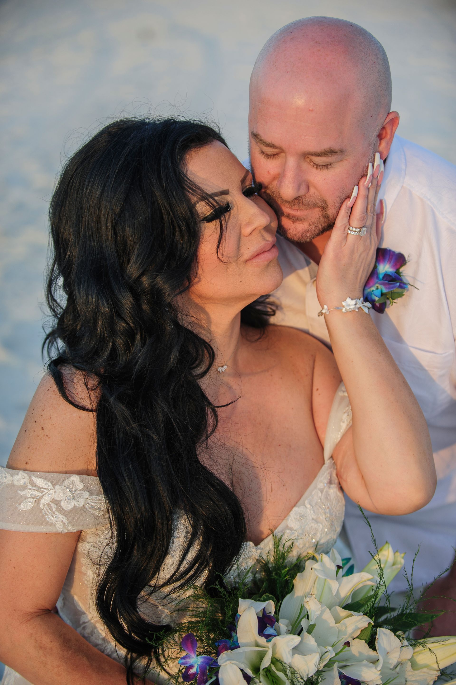 Couple embracing at a wedding, with the bride holding a white bouquet and touching the groom’s face.