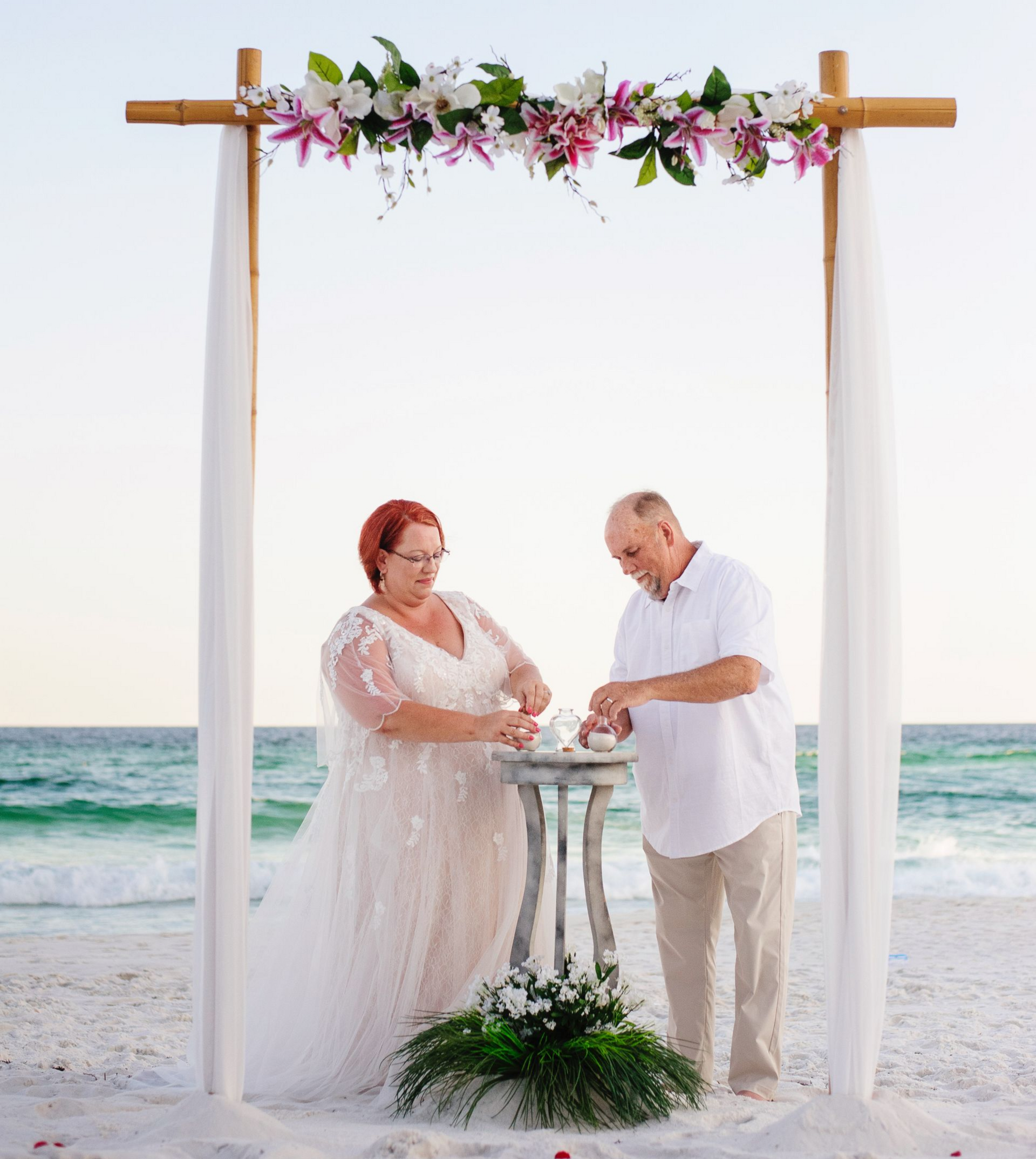 Couple exchanging vows at a beach wedding under a floral arch