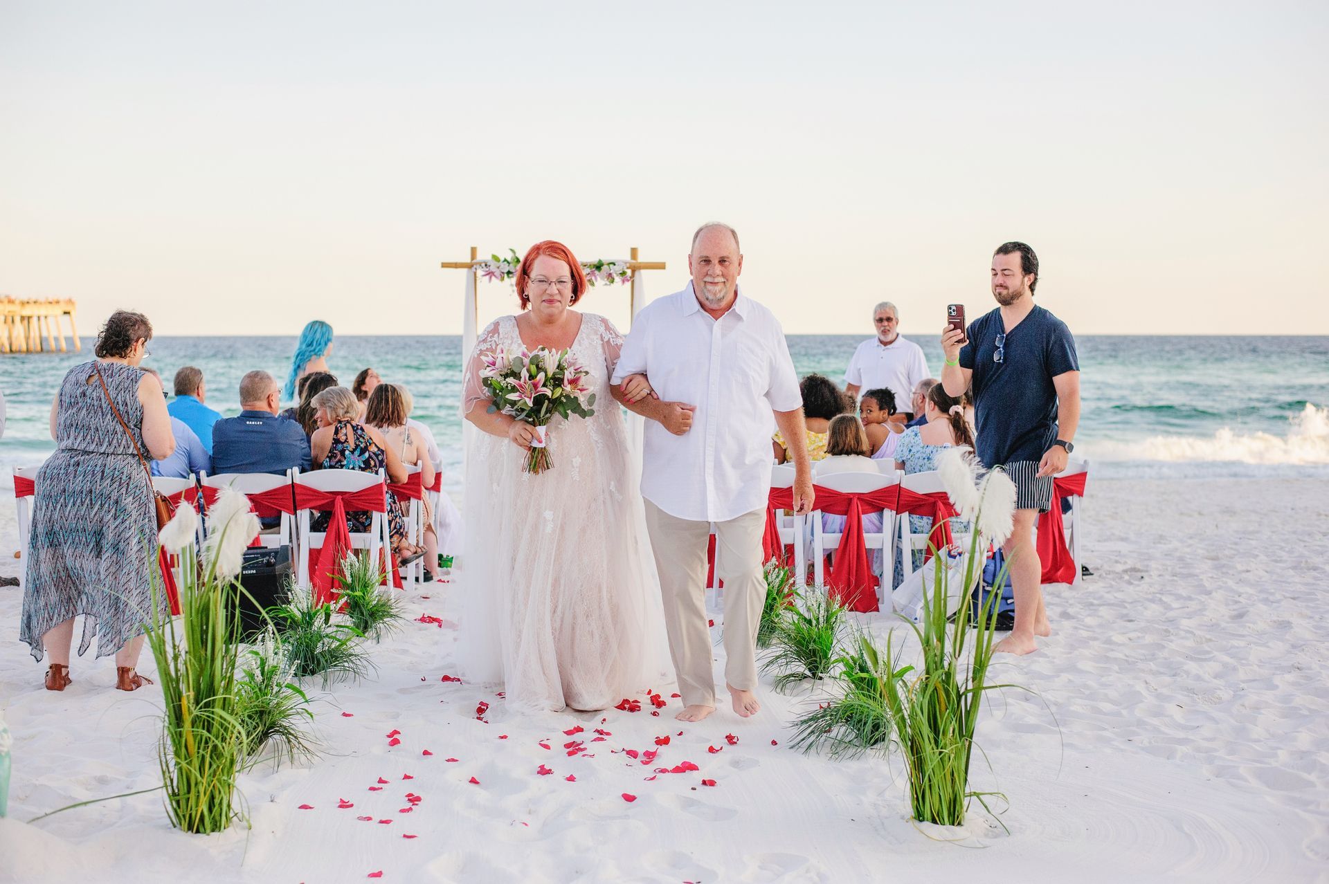 Beach wedding couple walking down aisle between seated guests at sunset