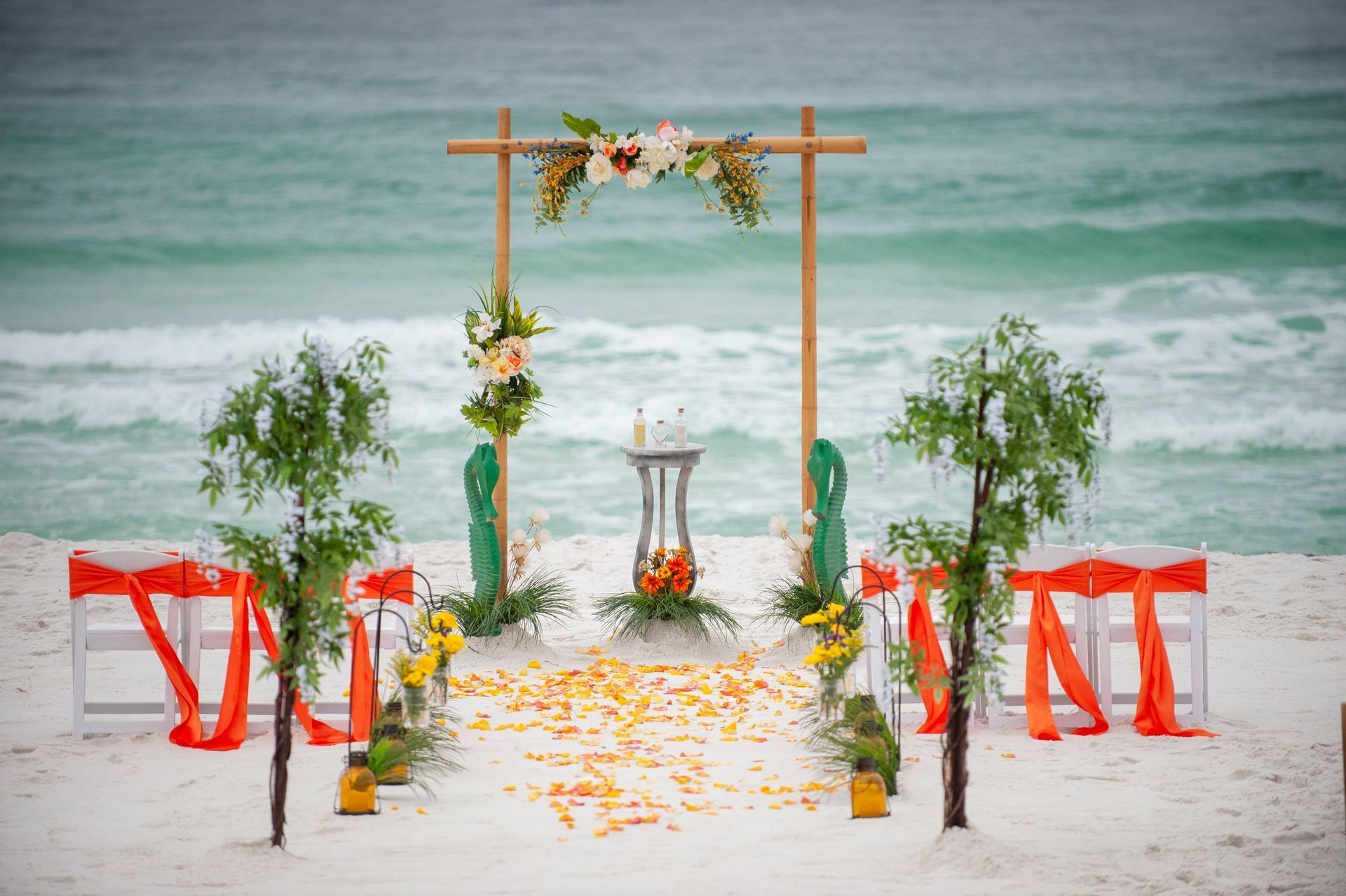 Beach wedding arch with white chairs, red ribbons, and floral decorations by the ocean