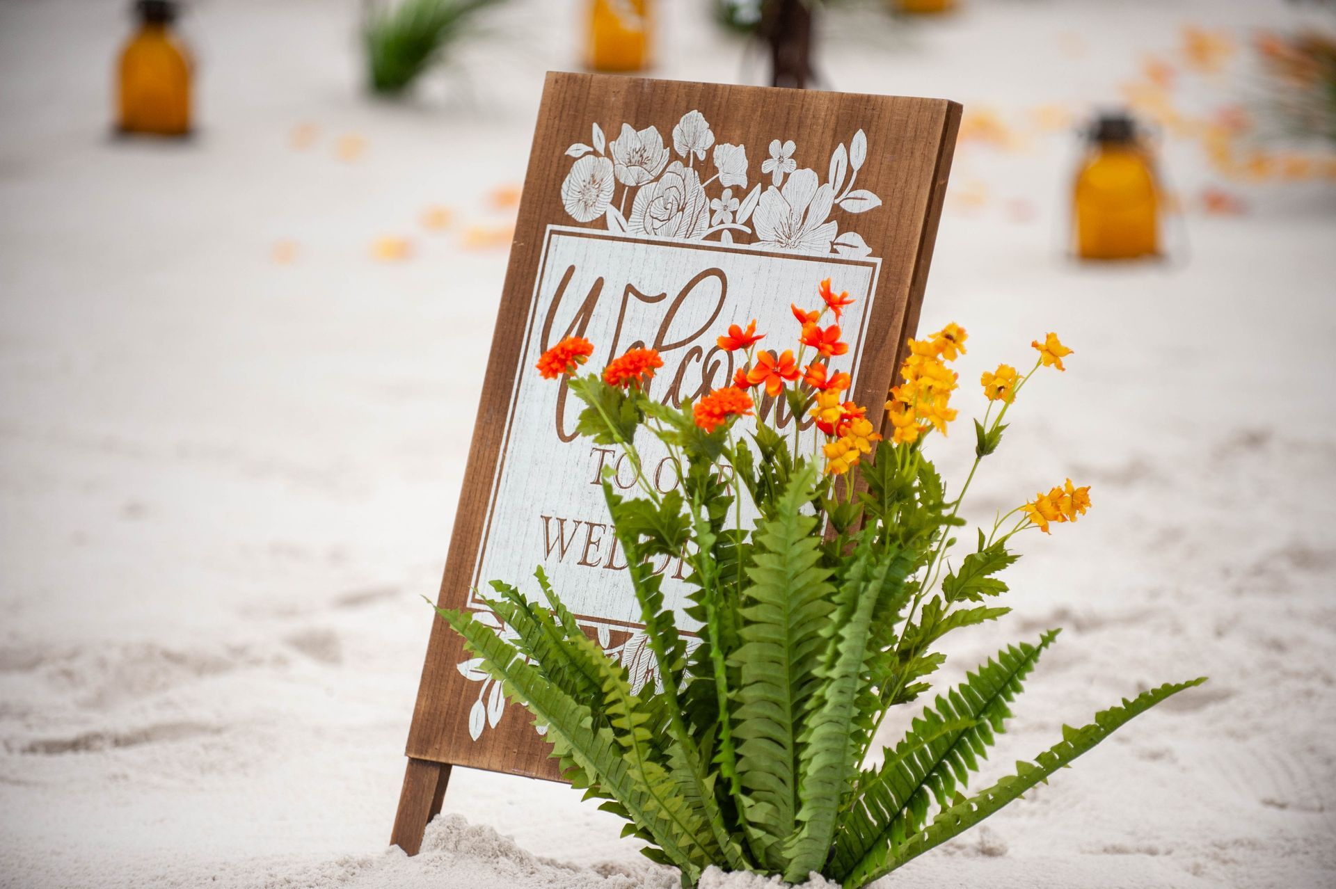 Wooden wedding sign with greenery and orange flowers on a sandy beach background