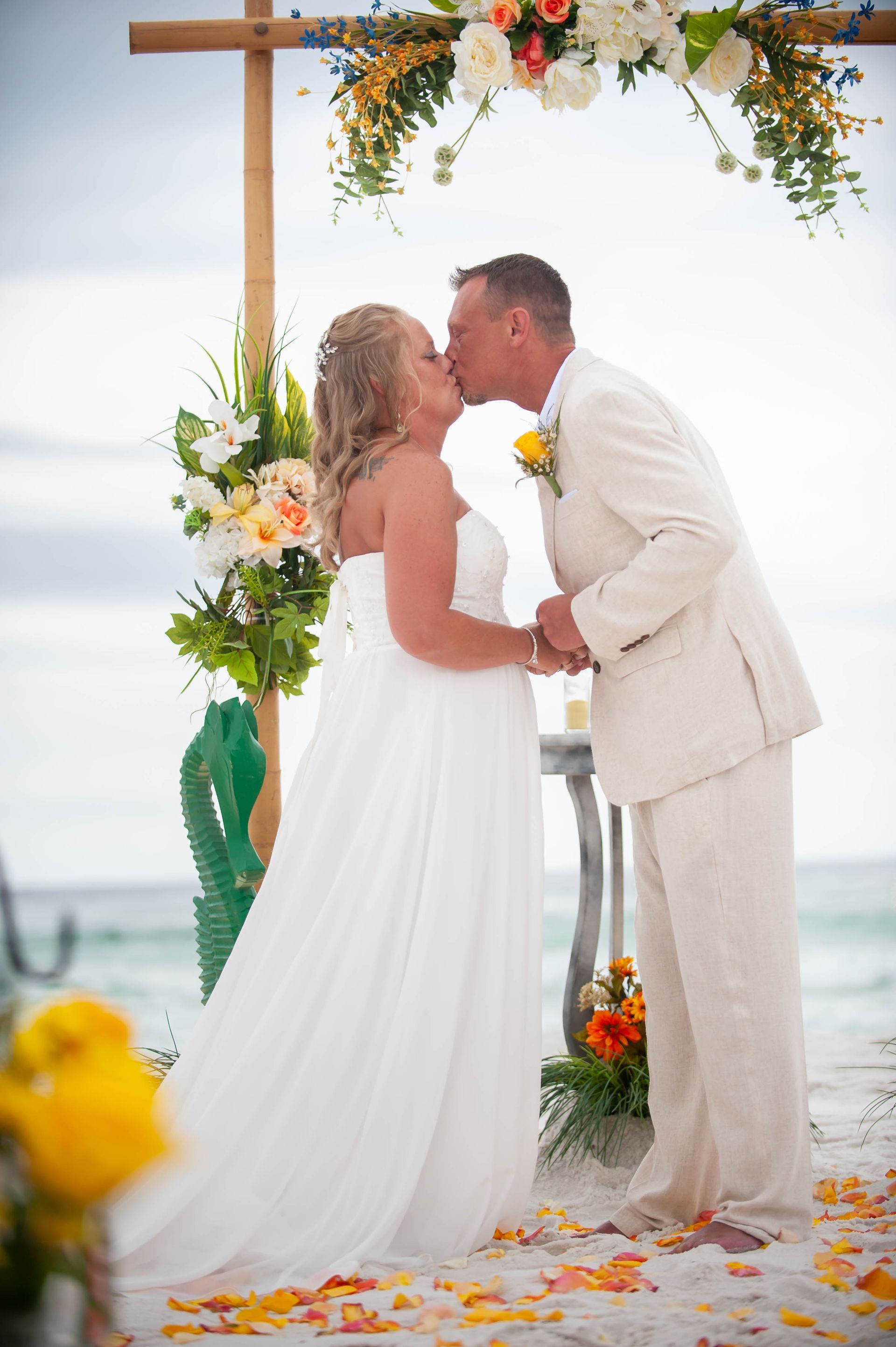 Couple kissing under a floral arch on a beach wedding altar