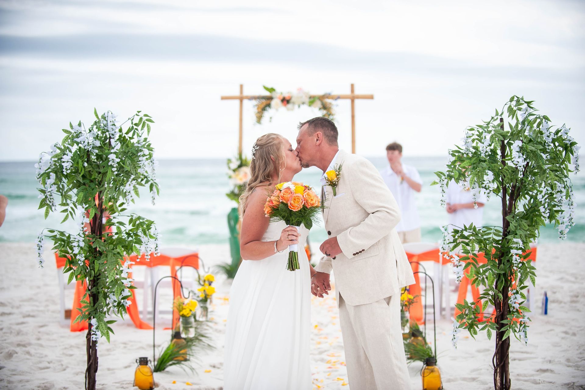 Bride and groom kissing under a floral arch on a bright beach wedding setup