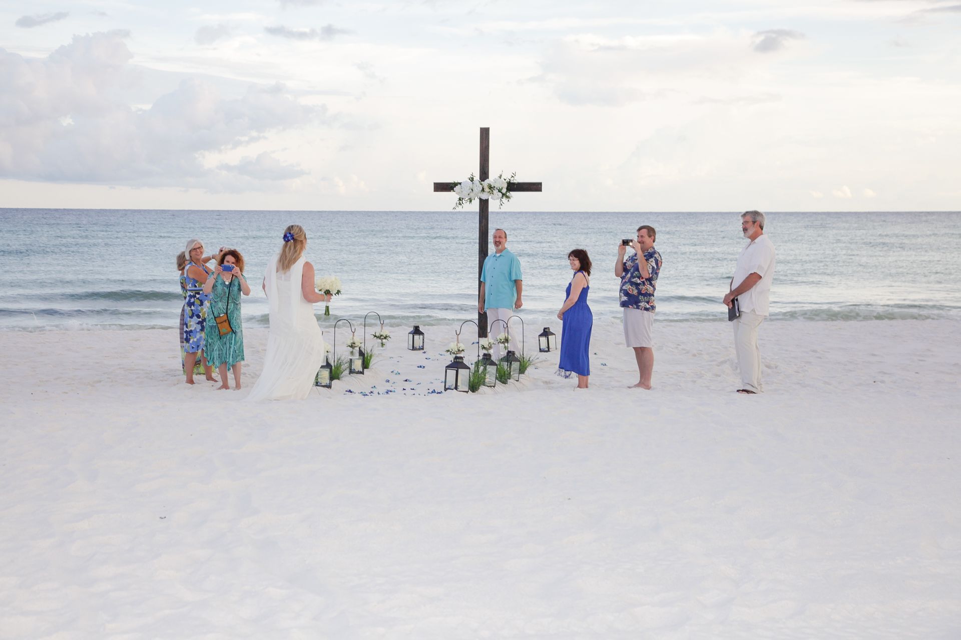 Small wedding ceremony on a white sandy beach with an arch and guests by the ocean