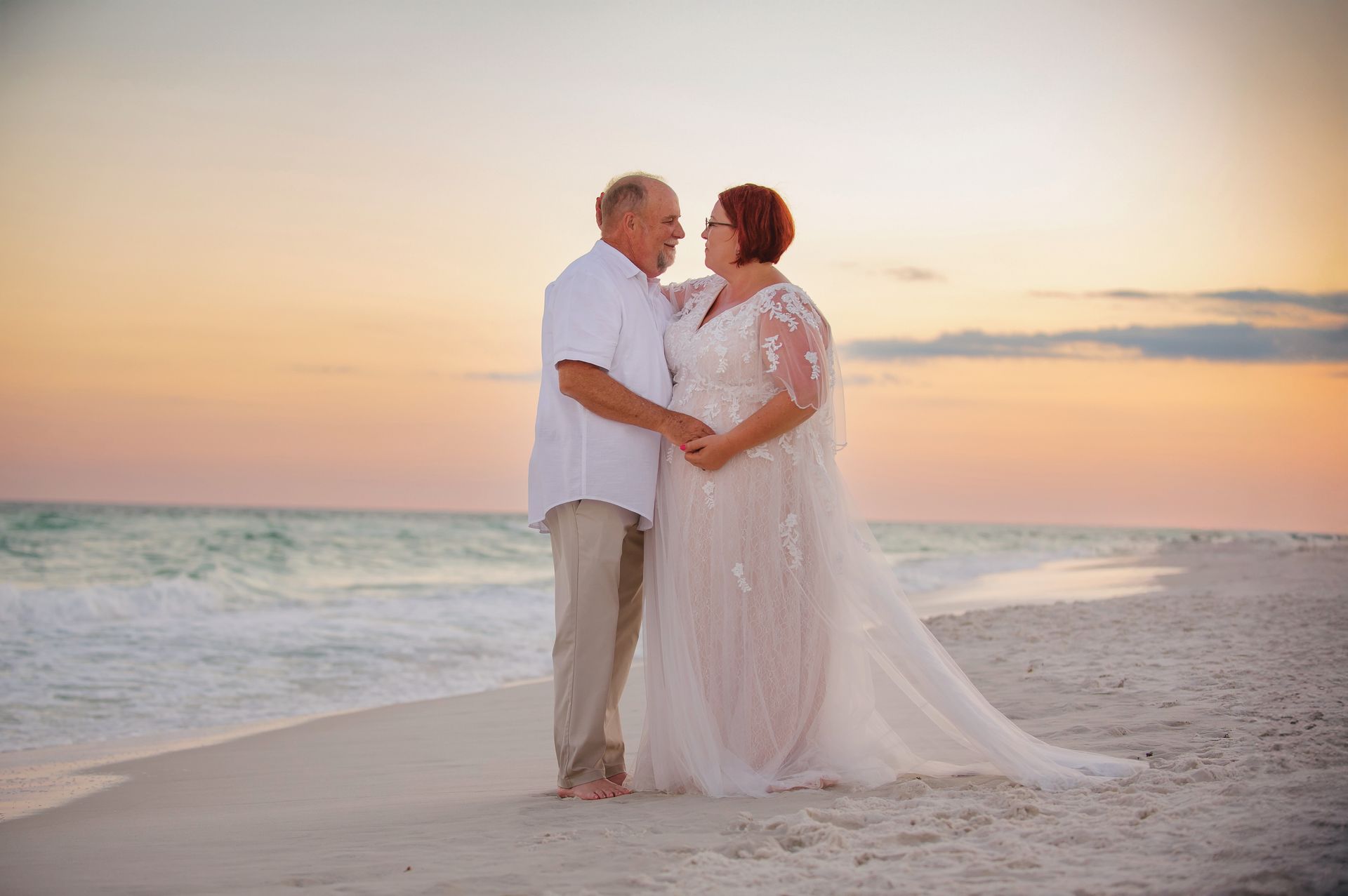 Two people embracing on a beach at sunset, with gentle waves and a pastel sky.