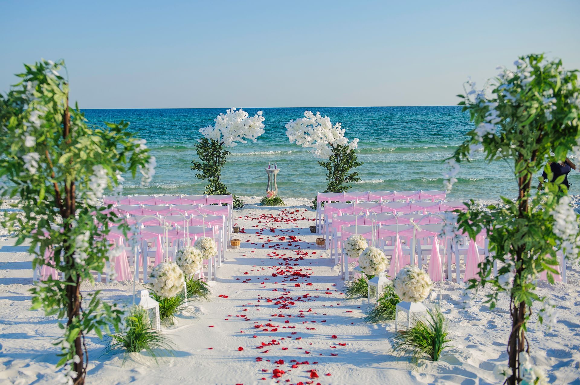 Outdoor beach wedding aisle with pink flowers and white chairs leading to the ocean
