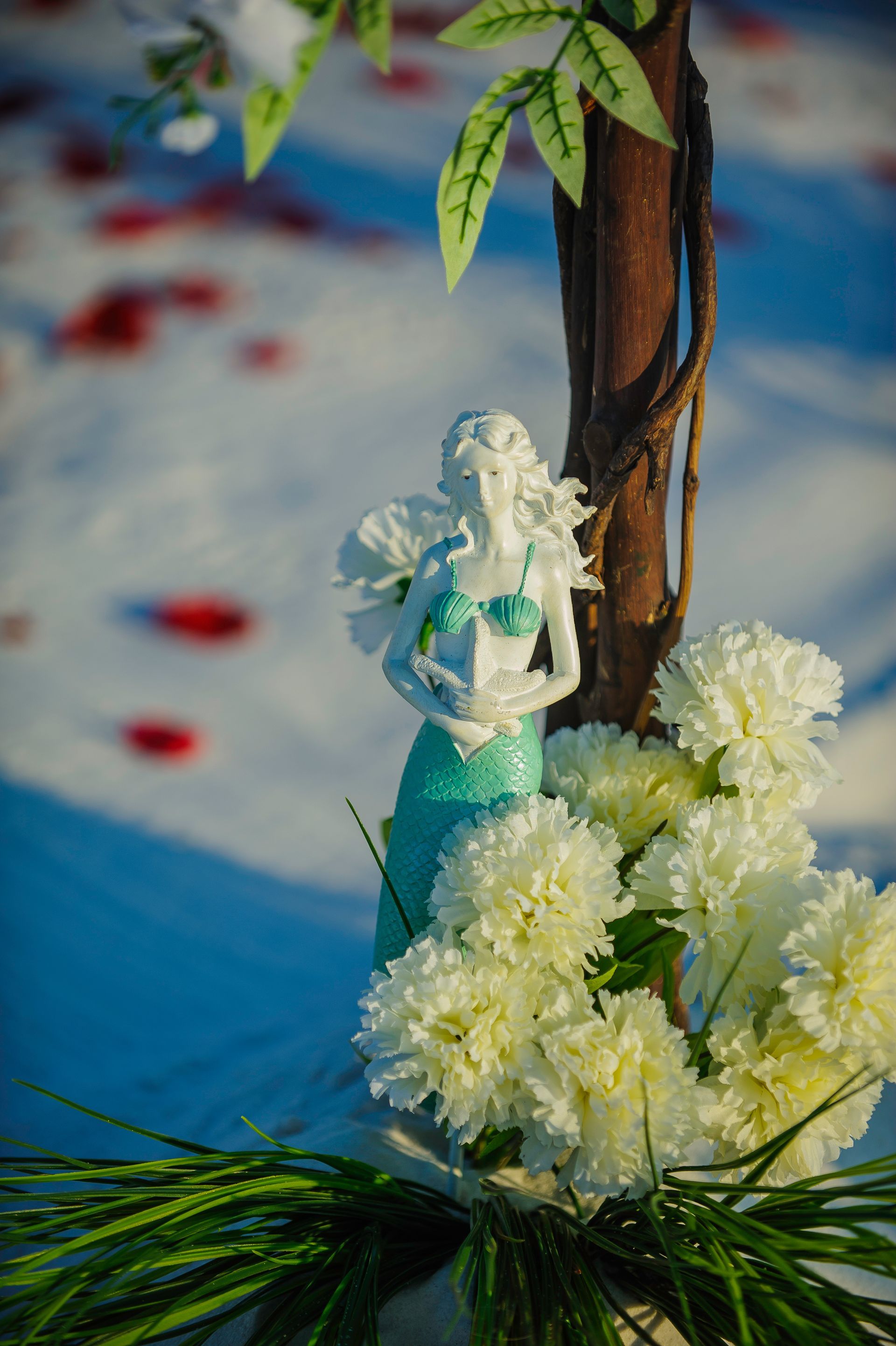 White floral arrangement with a small angel figurine tied to a tree trunk on a blue background