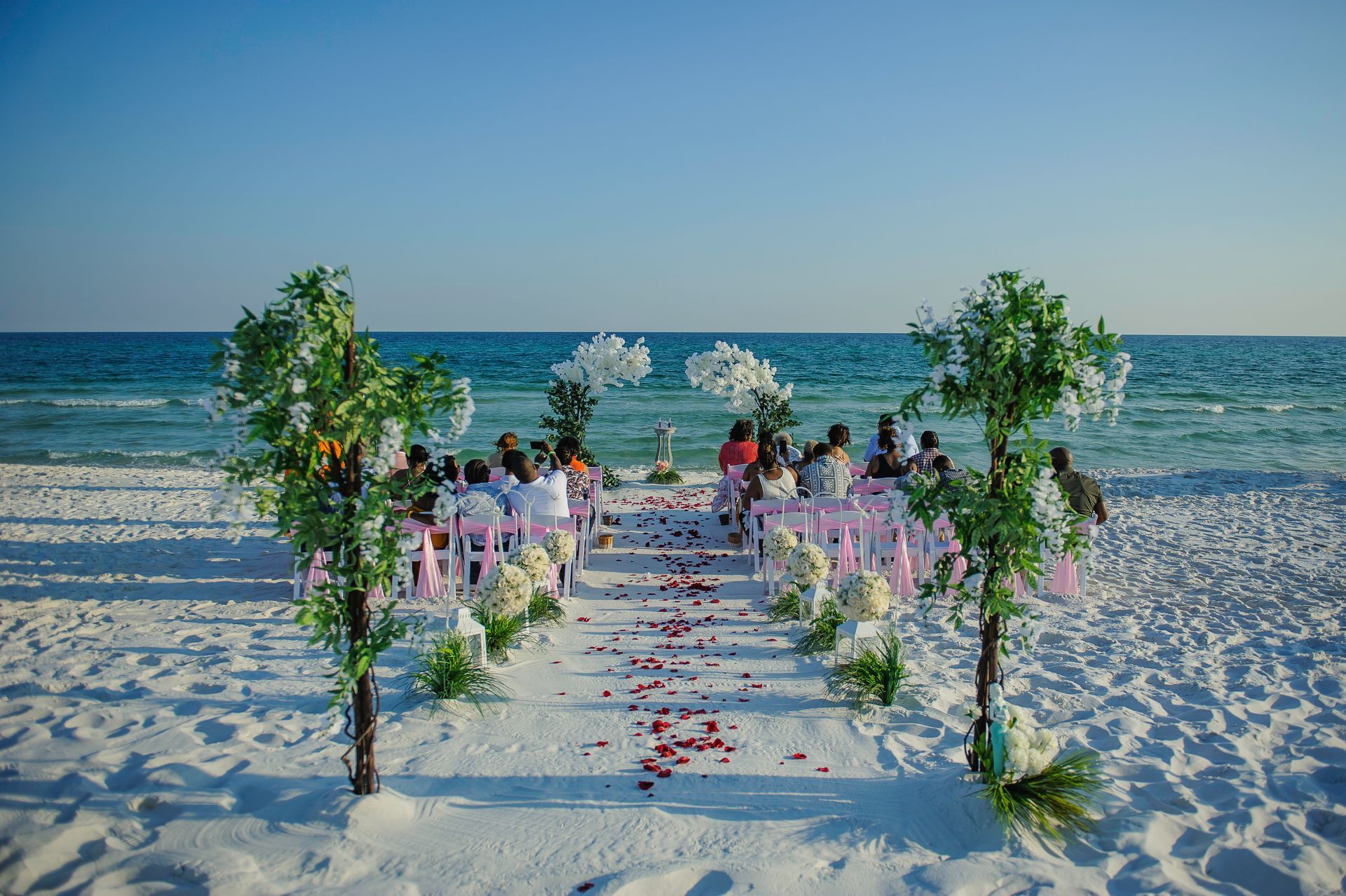 Beach wedding aisle decorated with flowers, leading to a small ceremony setup by the ocean