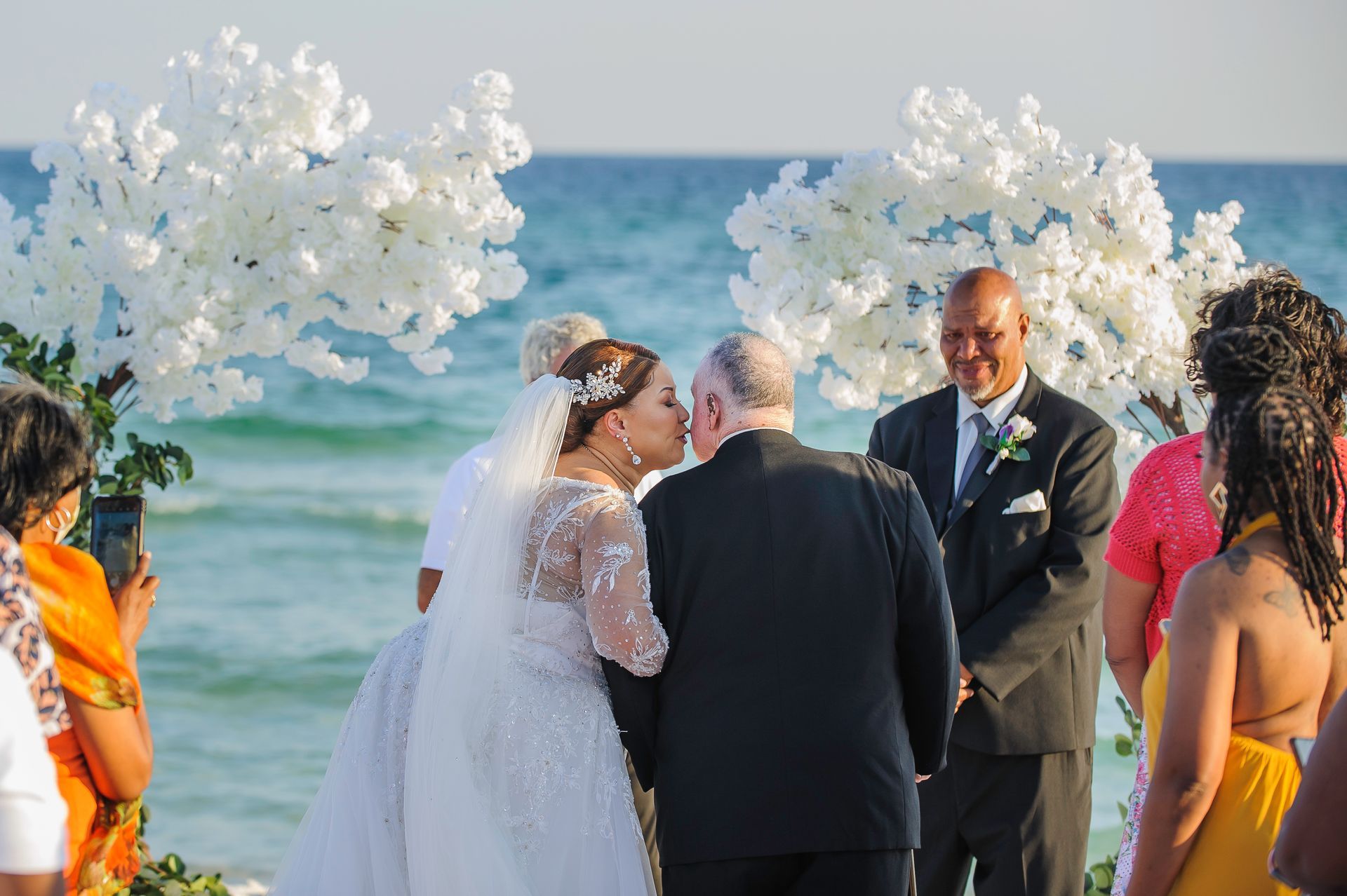 father kissing bride during beach wedding