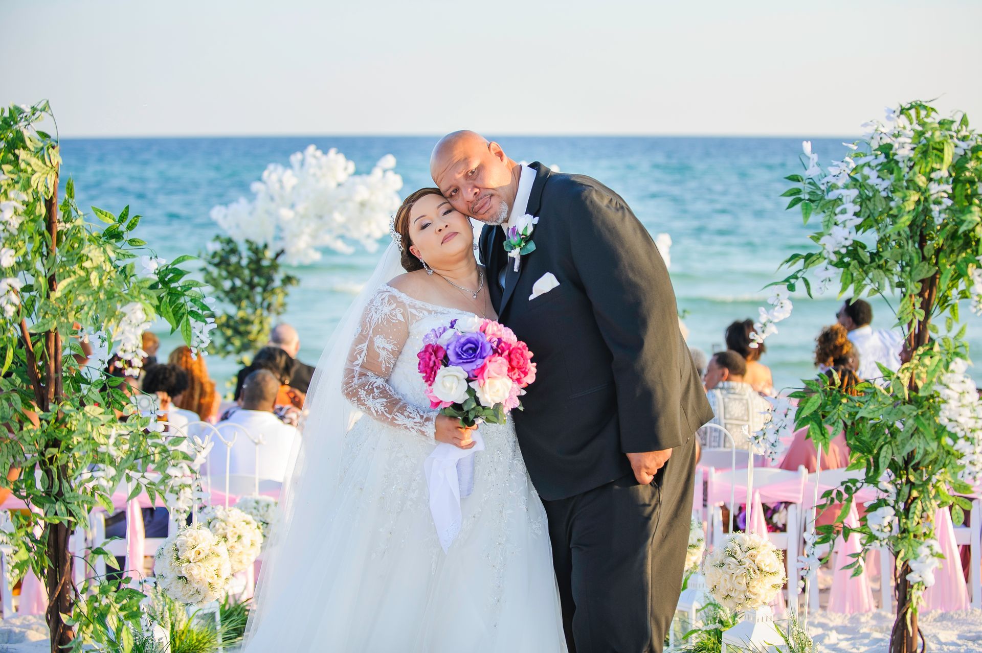 Newlyweds kissing under a floral arch at a beach wedding ceremony