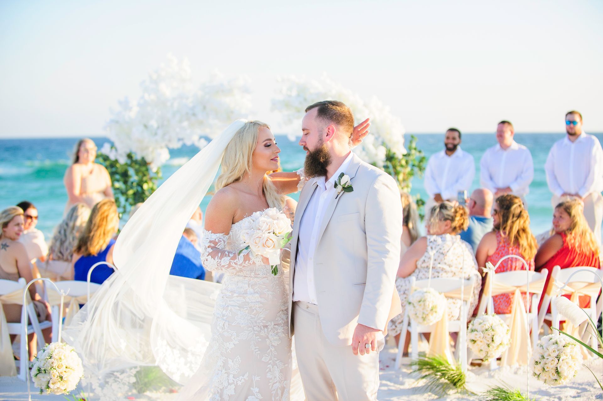 Bride and groom kiss at an outdoor beach wedding with guests seated behind them