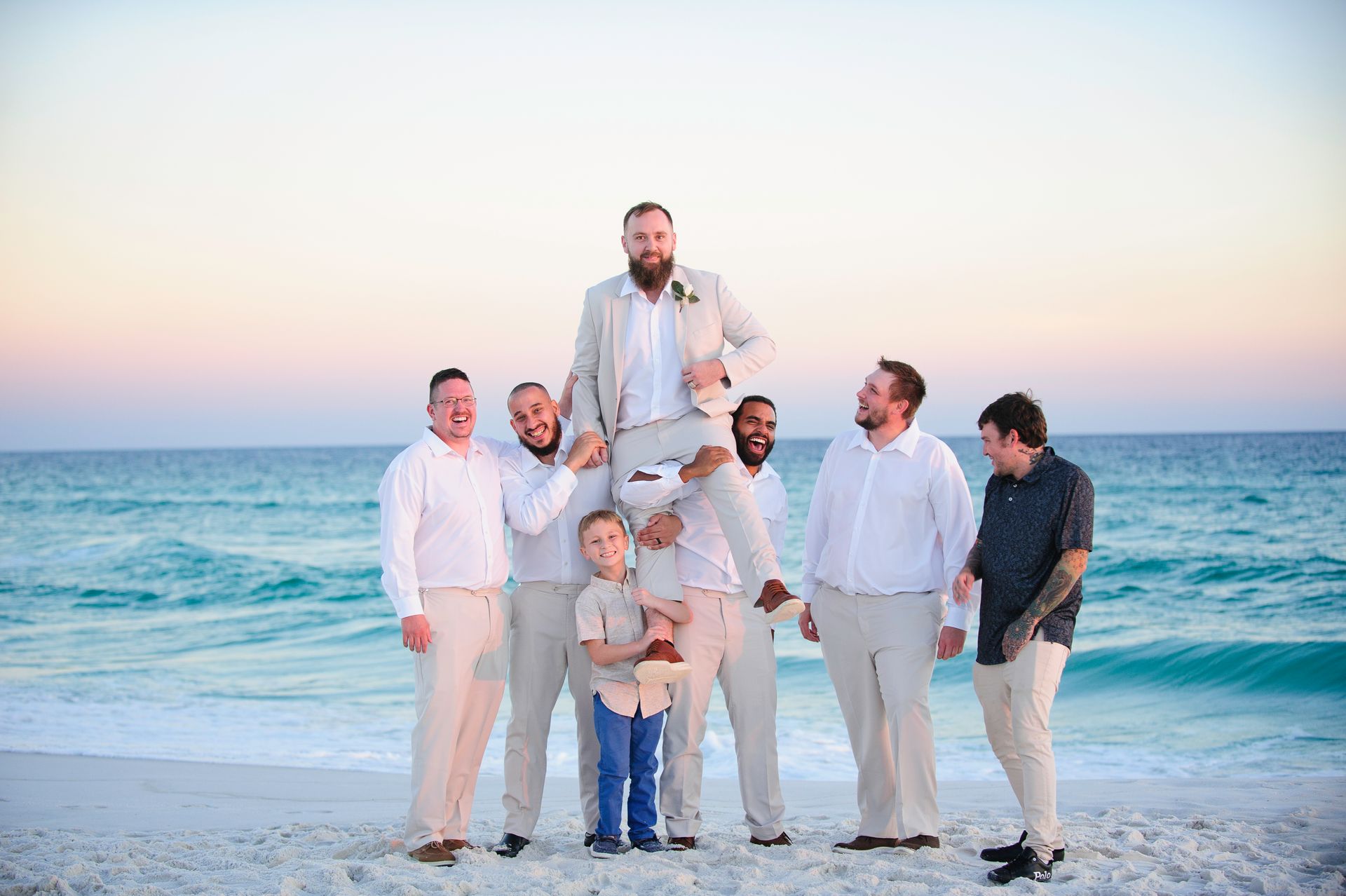 Group of seven people posing on a beach at sunset, with ocean waves behind them.