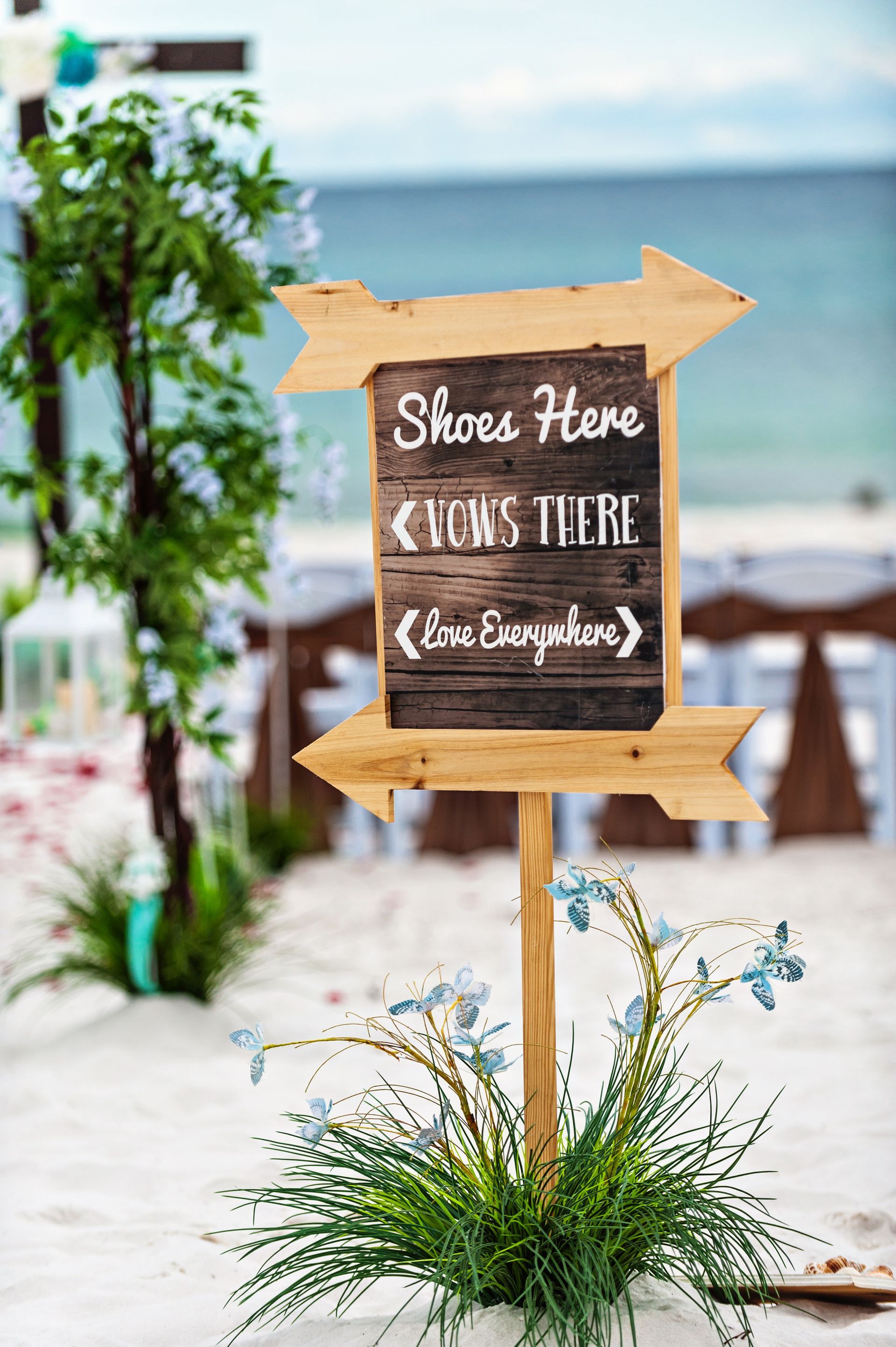 Beach wedding sign with wooden arrow pointing right, reading “Share Here & I Do’s Here” on a seaside path.