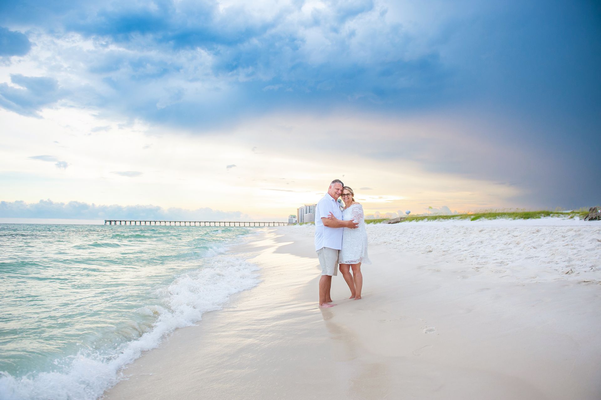 Couple walking hand in hand along a white sandy beach under a cloudy sky at sunset