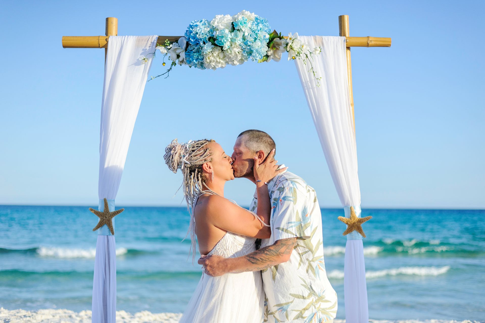 bride and groom kissing under tropical arch during beach wedding