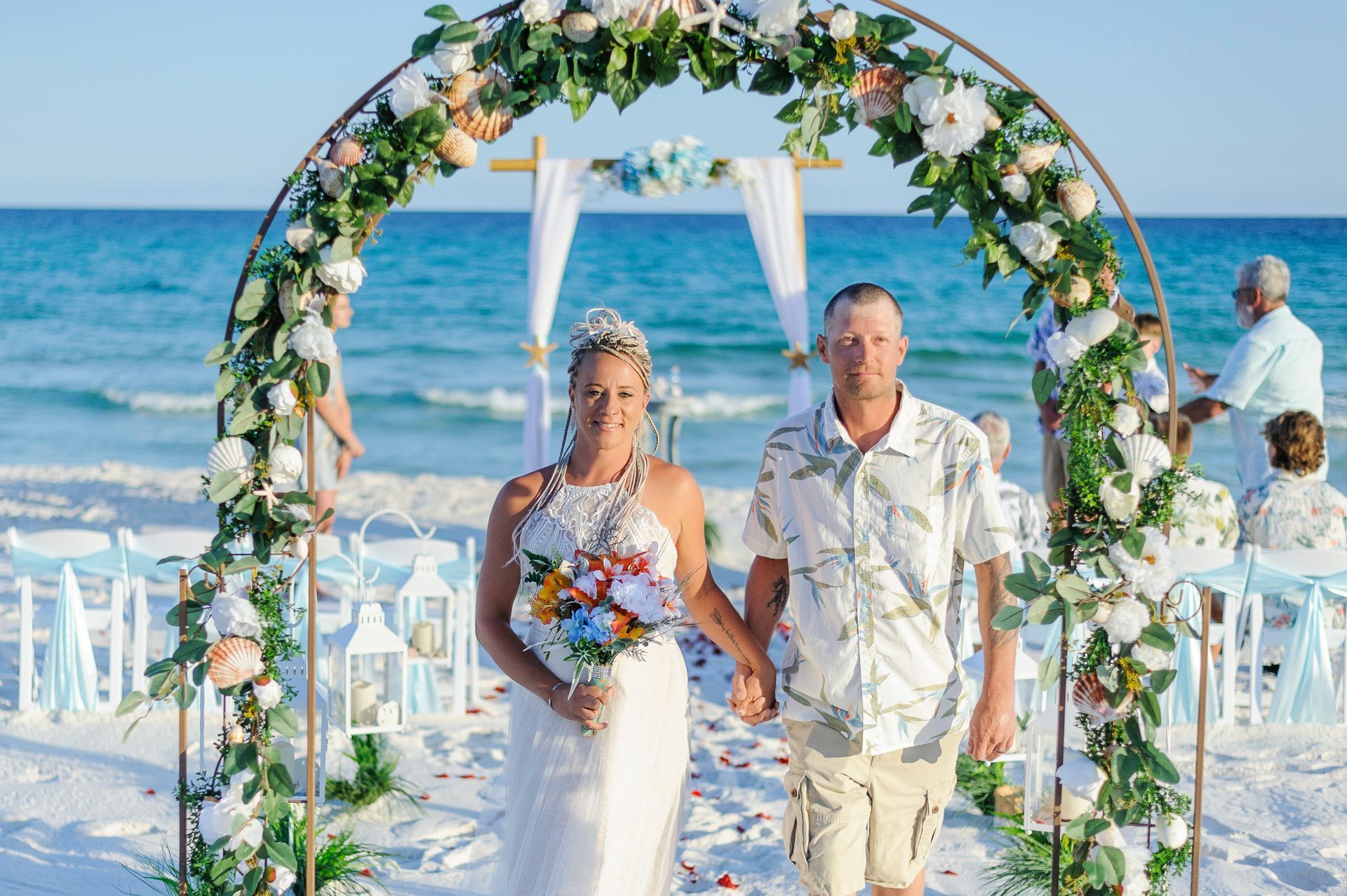 bride and groom walking under floral arch during beach wedding