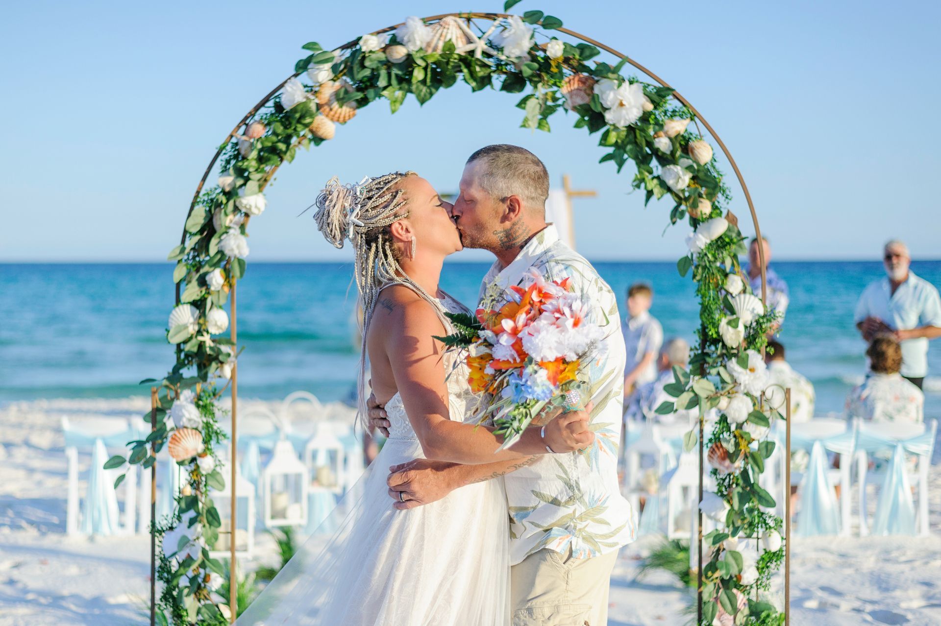Couple kissing under a floral arch on a beach wedding aisle by the ocean