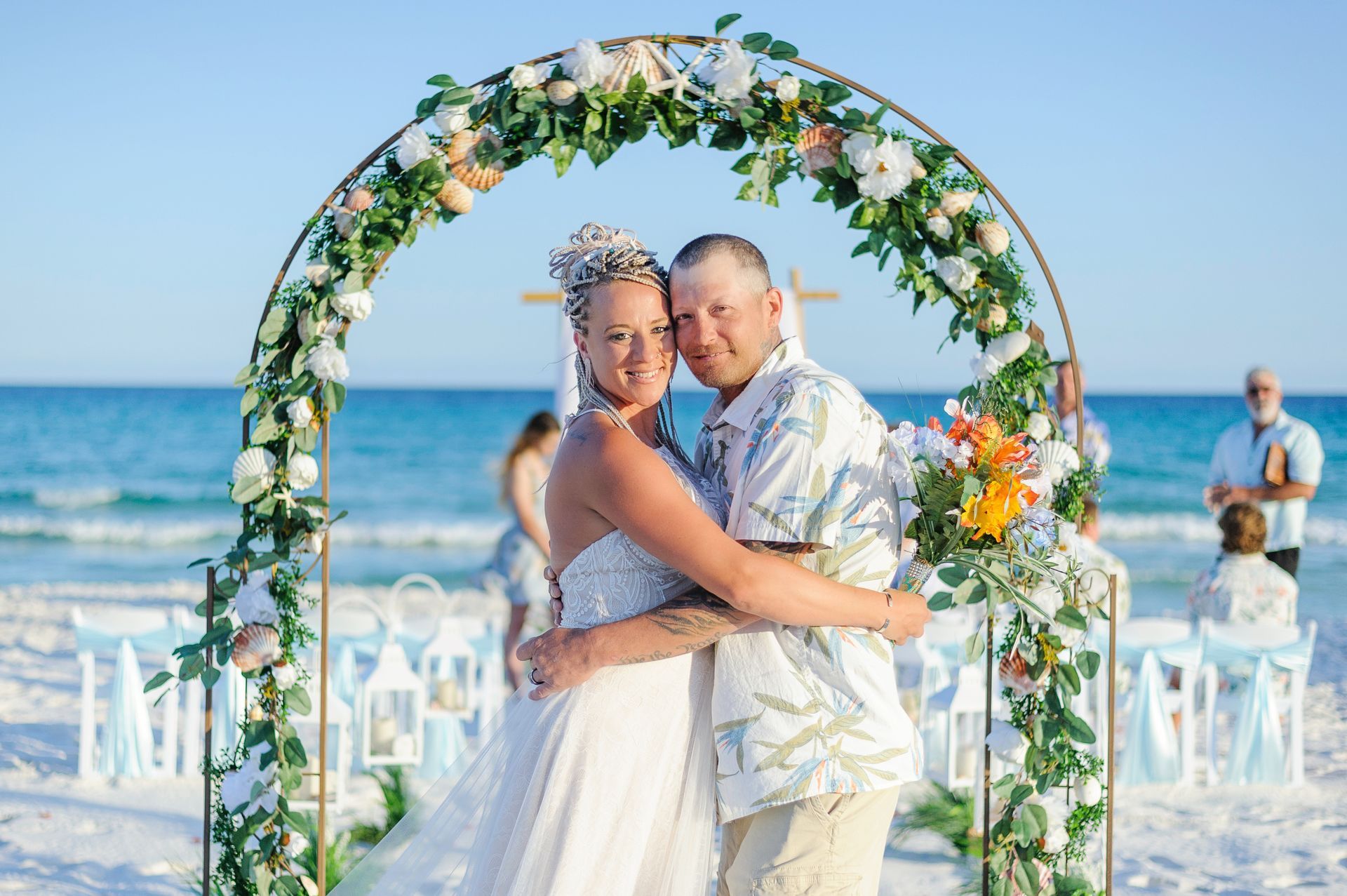 Couple embracing under a flower arch on a beach wedding aisle by the ocean