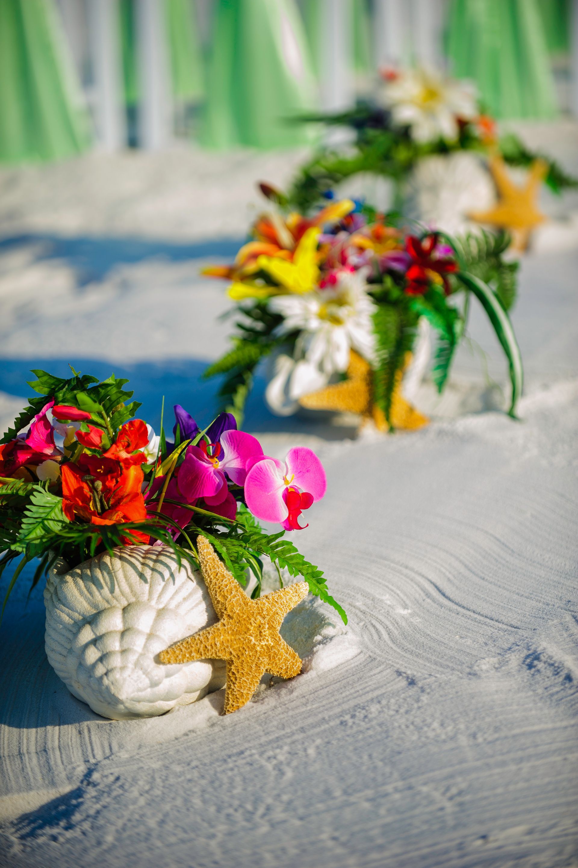 Decorative seashell bouquets with colorful flowers and starfish on a white sandy beach