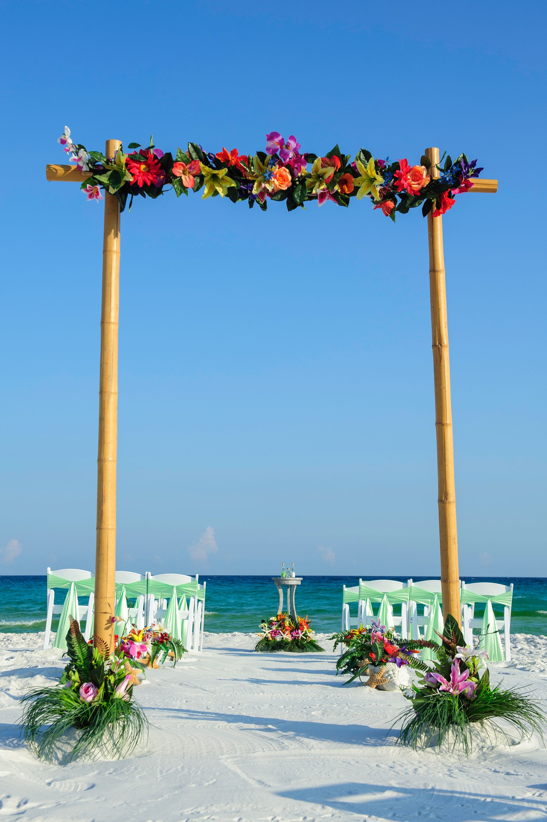Beach wedding arch with colorful flowers on white sand by the turquoise sea