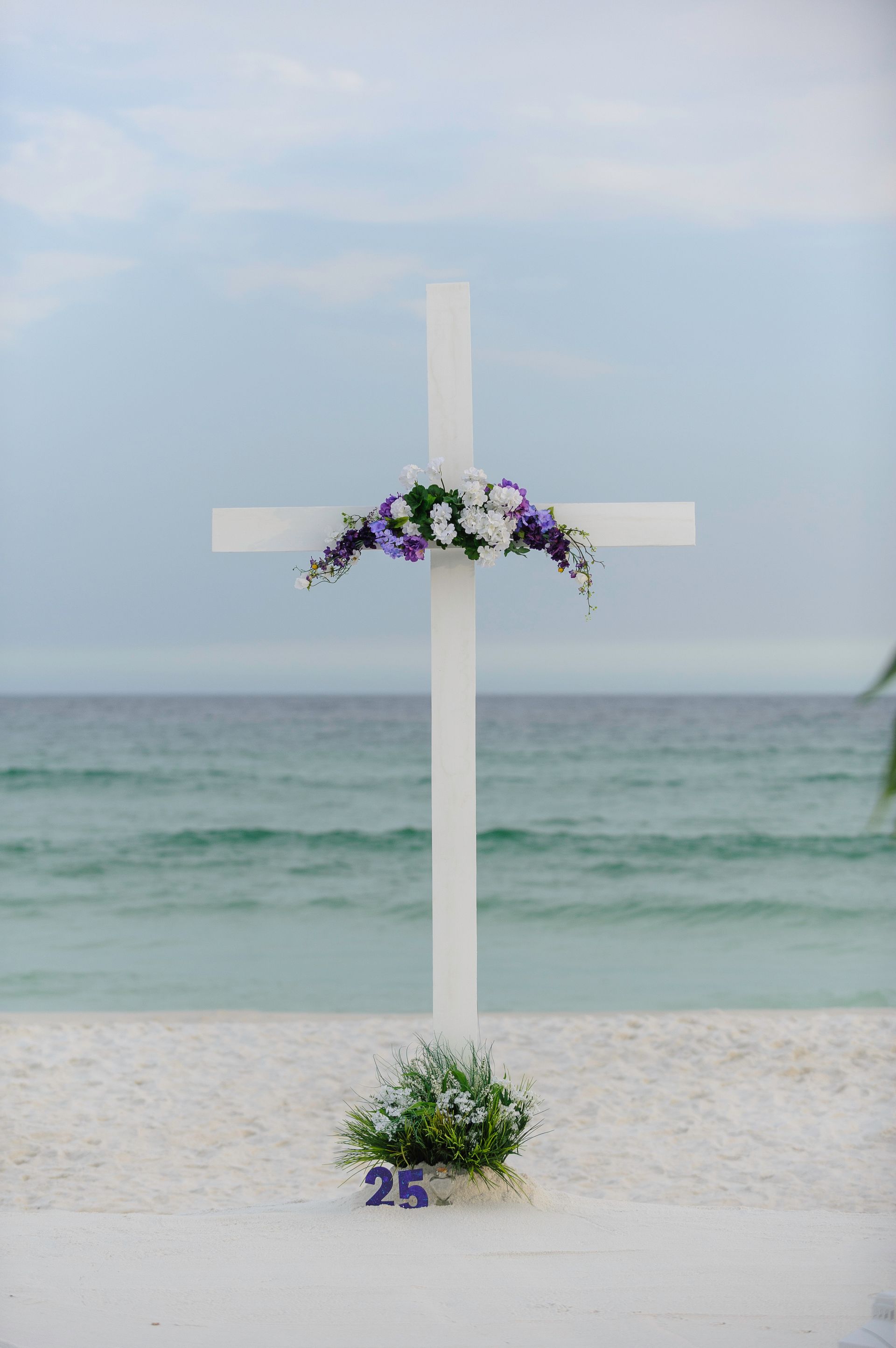 White cross with flowers on a beach by the sea under a cloudy sky