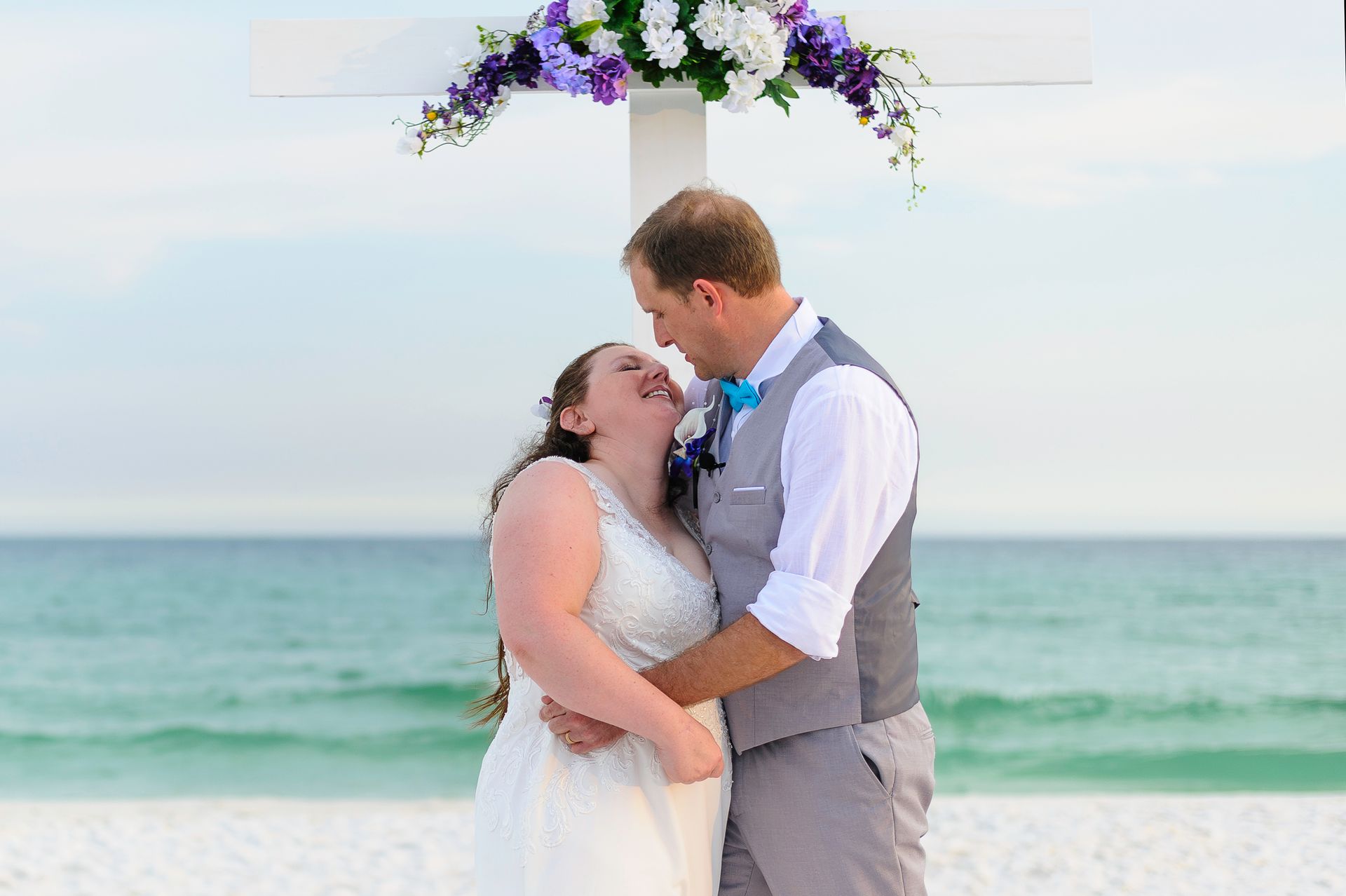 bride and groom standing under cross altar during beach wedding 