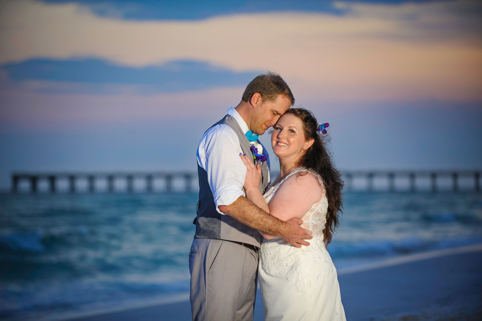 Couple embracing on a beach at sunset with a pier in the background