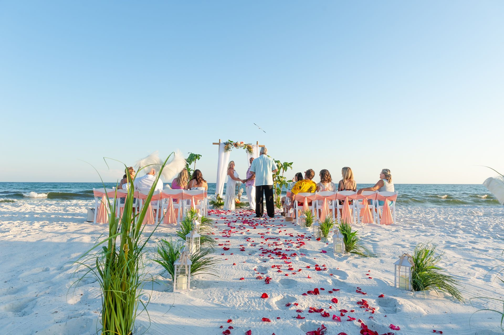 Beach wedding ceremony on a flower-strewn aisle with guests seated beside the ocean