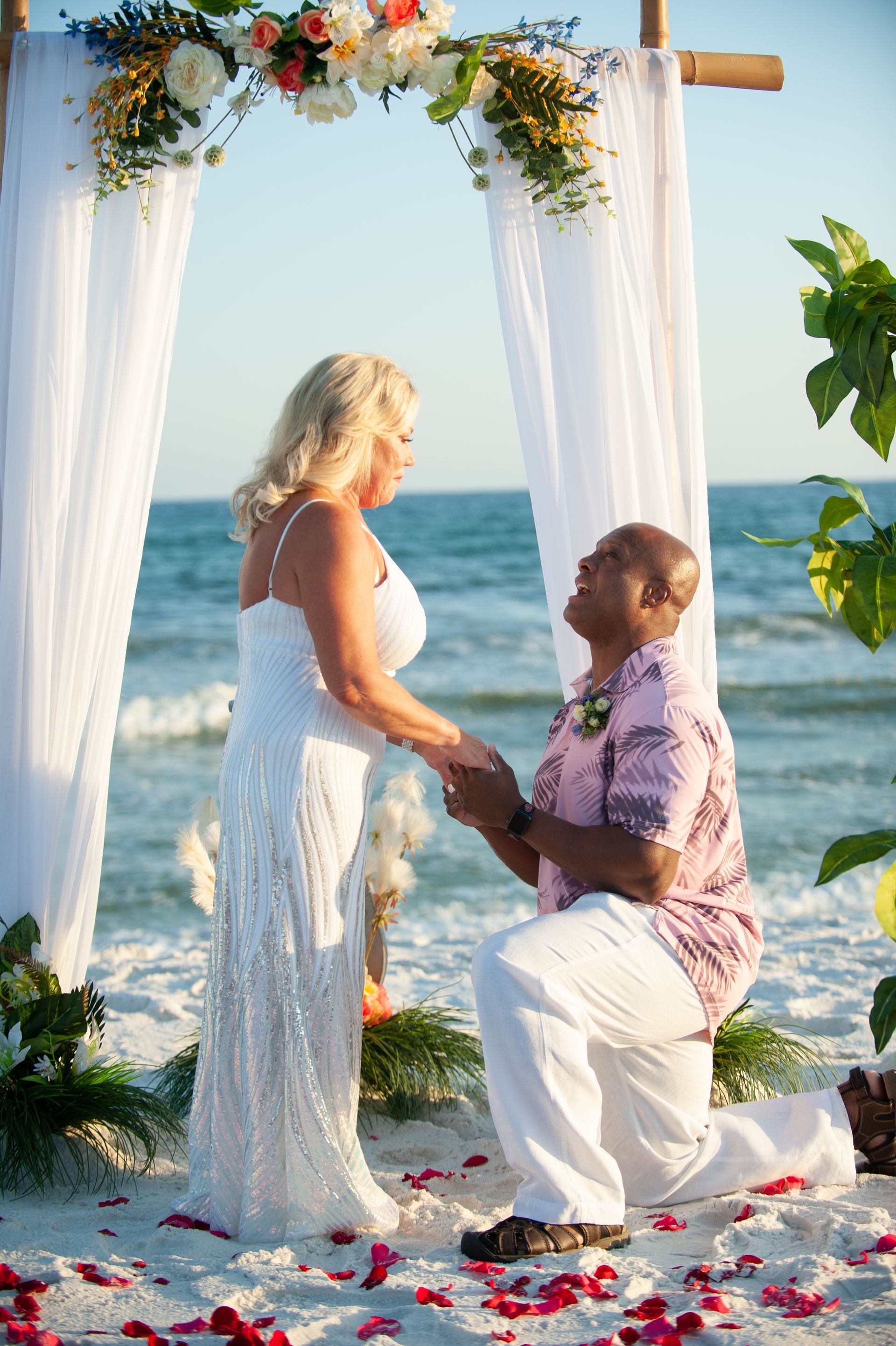 Couple exchanging vows under a flower arch on a beach at sunset