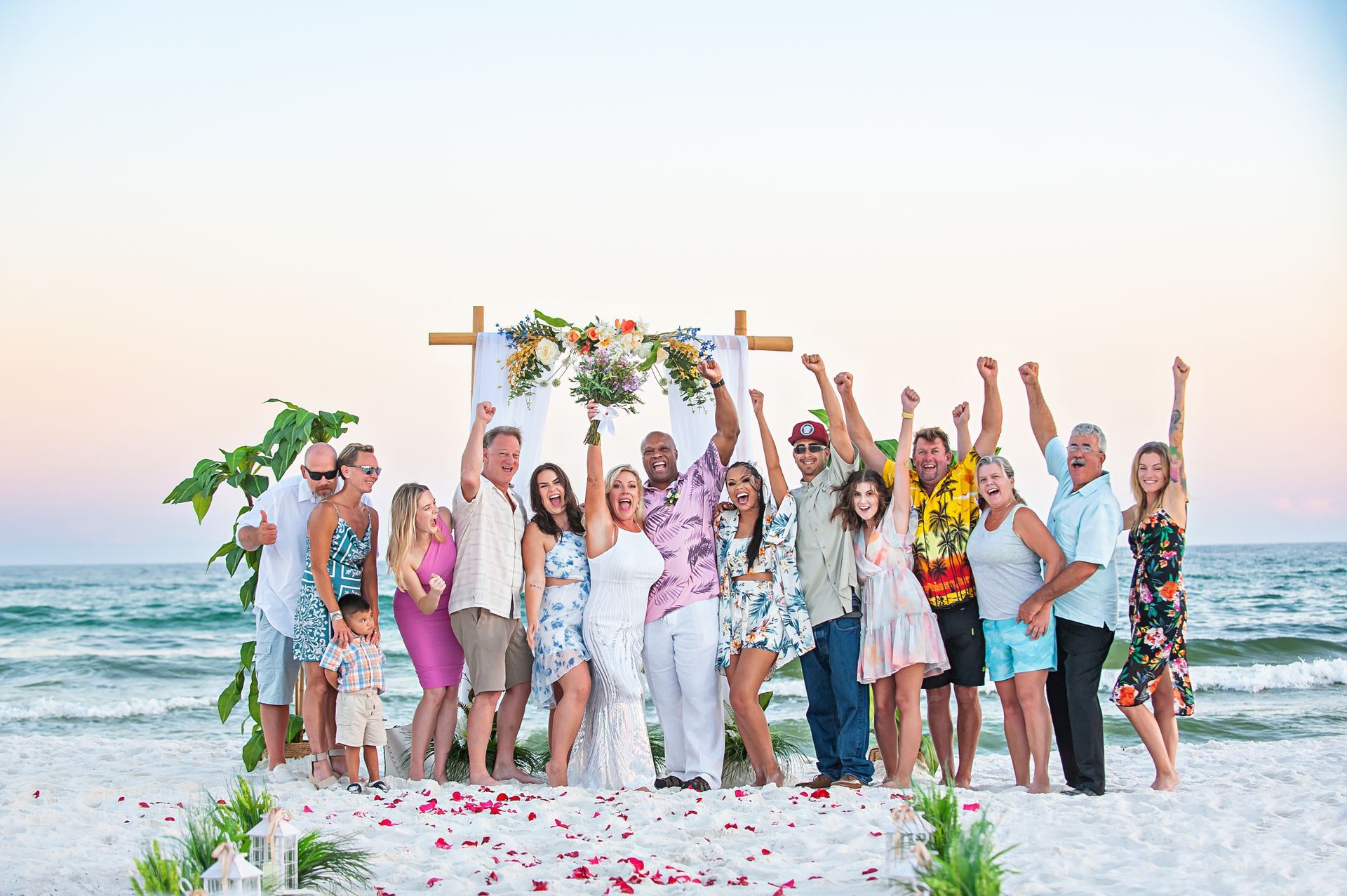 Group celebrating on a beach wedding altar, throwing confetti at sunset