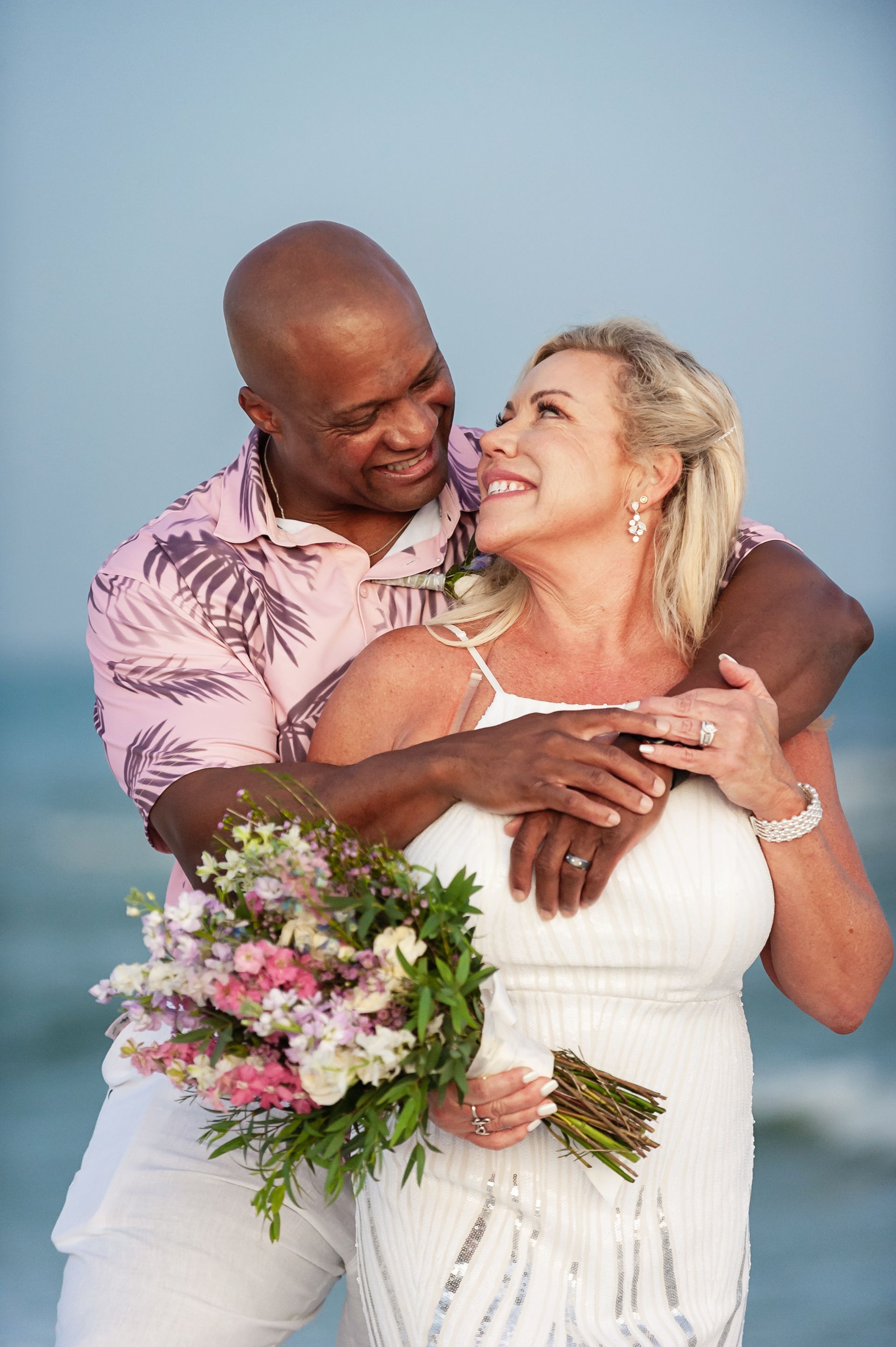 Couple embracing and smiling, with the woman holding a bouquet against a light blue backdrop.