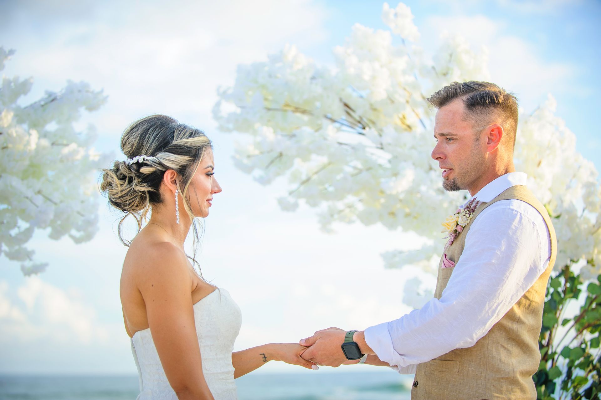 Bride and groom holding hands during an outdoor wedding ceremony under white flowering trees.