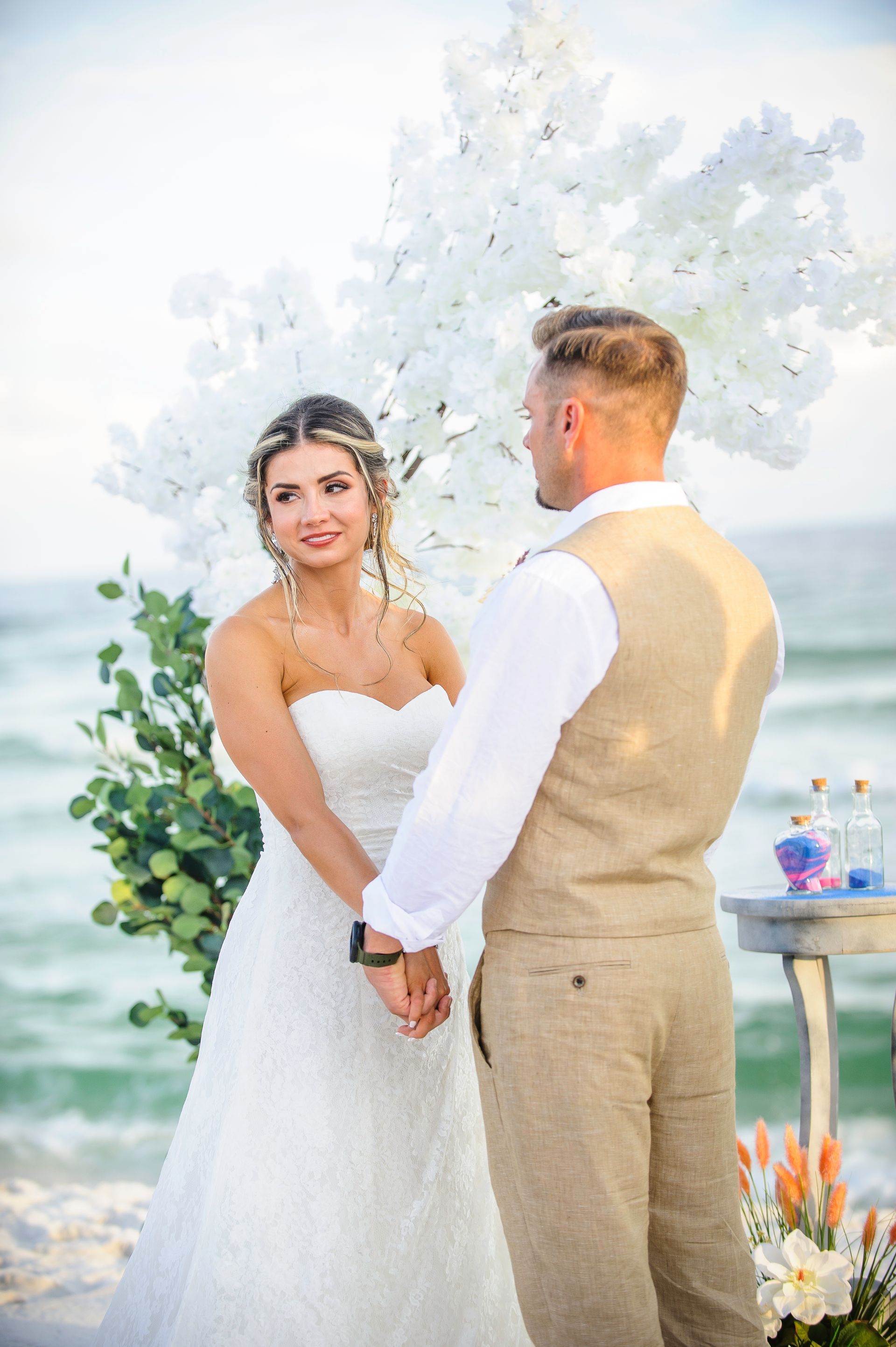 Bride and groom exchanging vows by the water in a white floral wedding ceremony