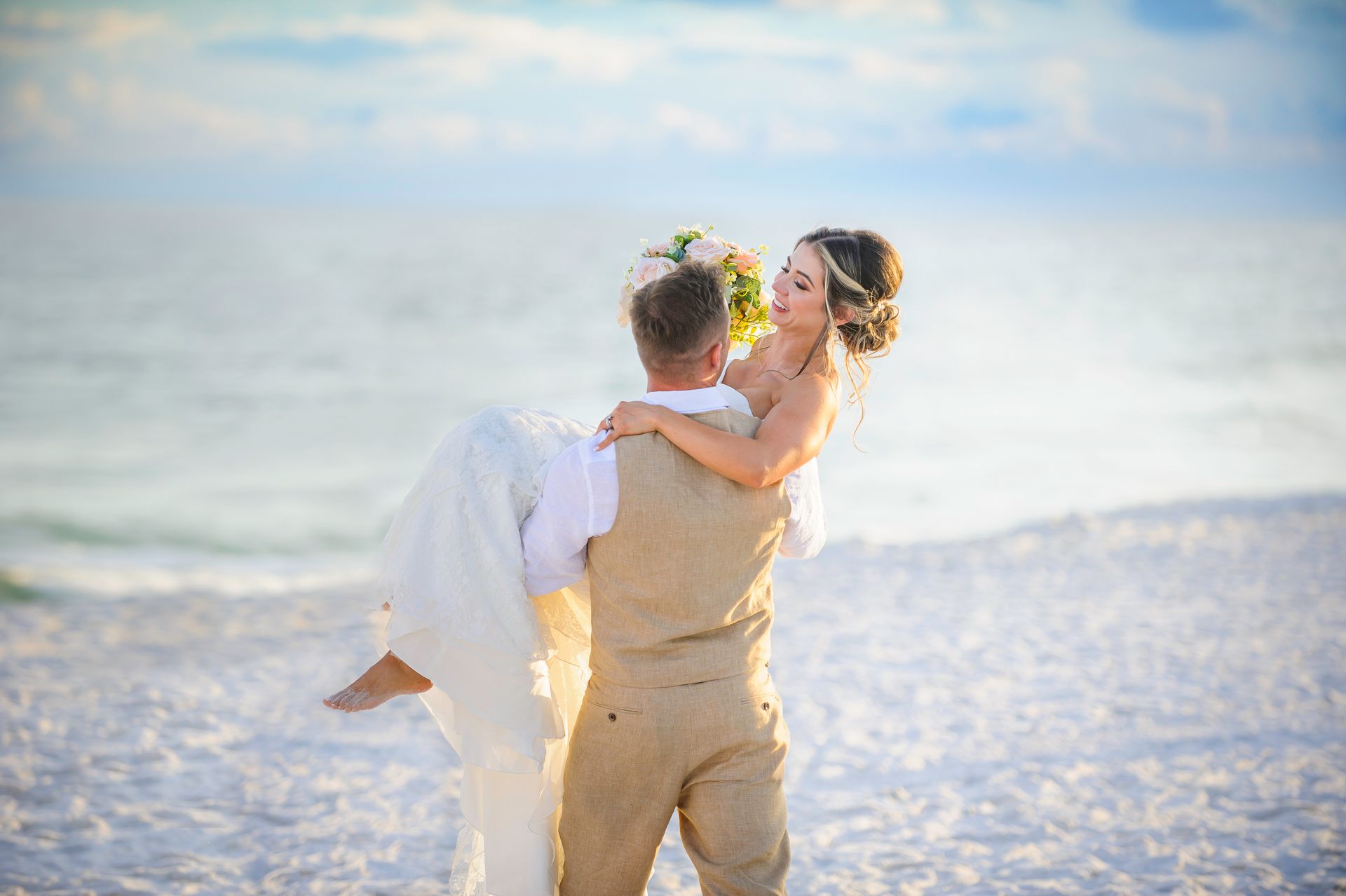 groom carrying bride across the beach